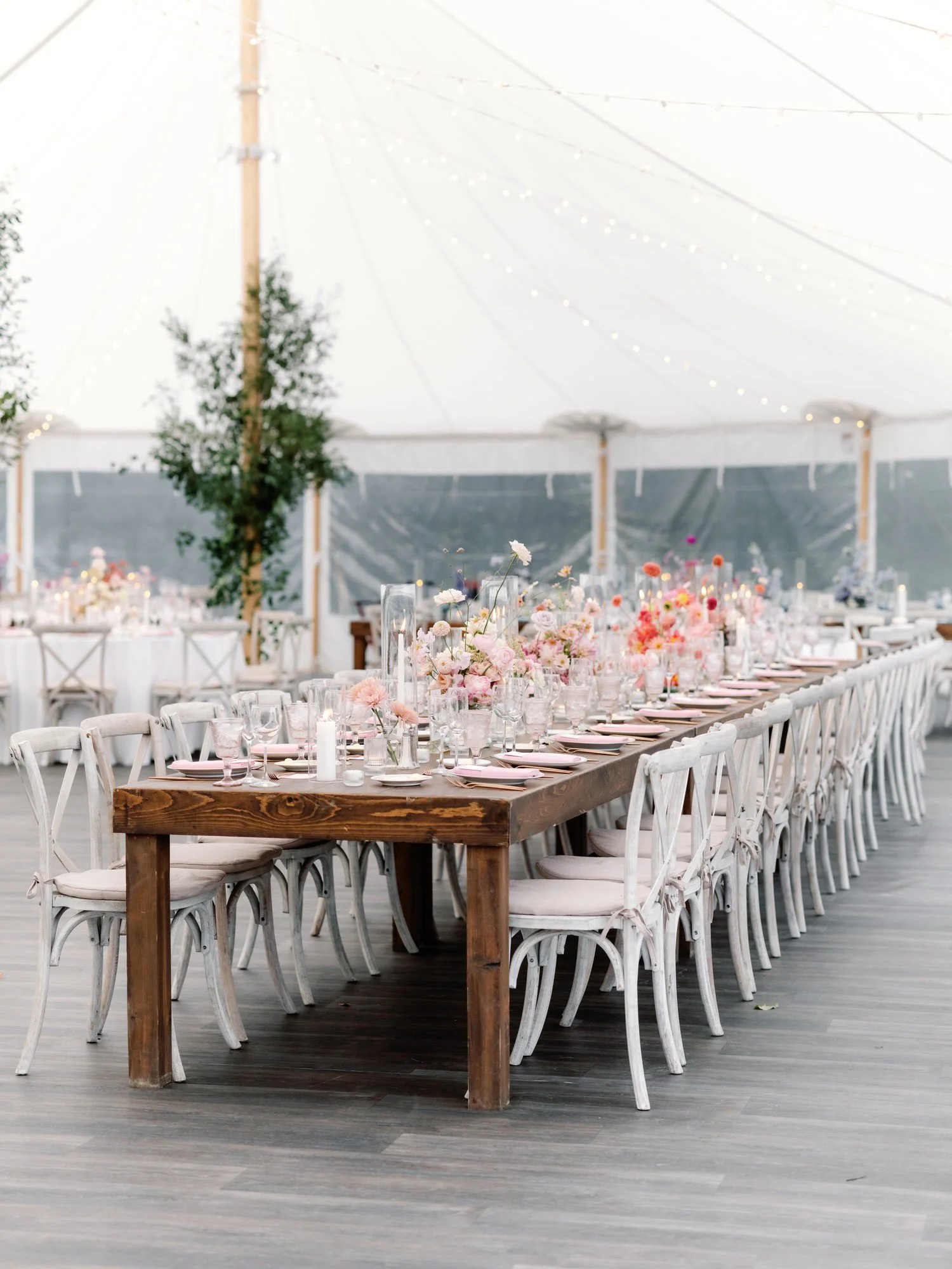 Reception tablescape with long wooden tables and pastel floral centerpieces inside tented wedding at The Ausable Club in the Adirondacks