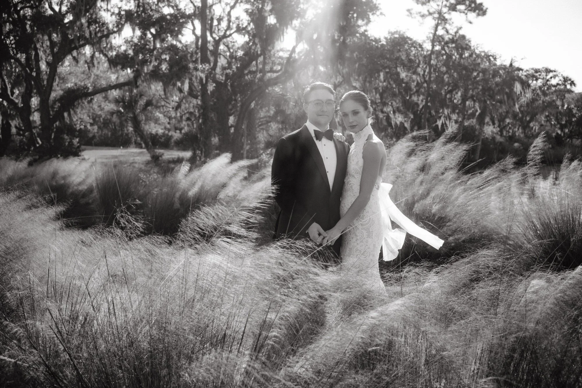 Bride and groom standing close together in a field of soft grass and sunlight at The Dunlin, Auberge, photographed by Jenny Fu.
