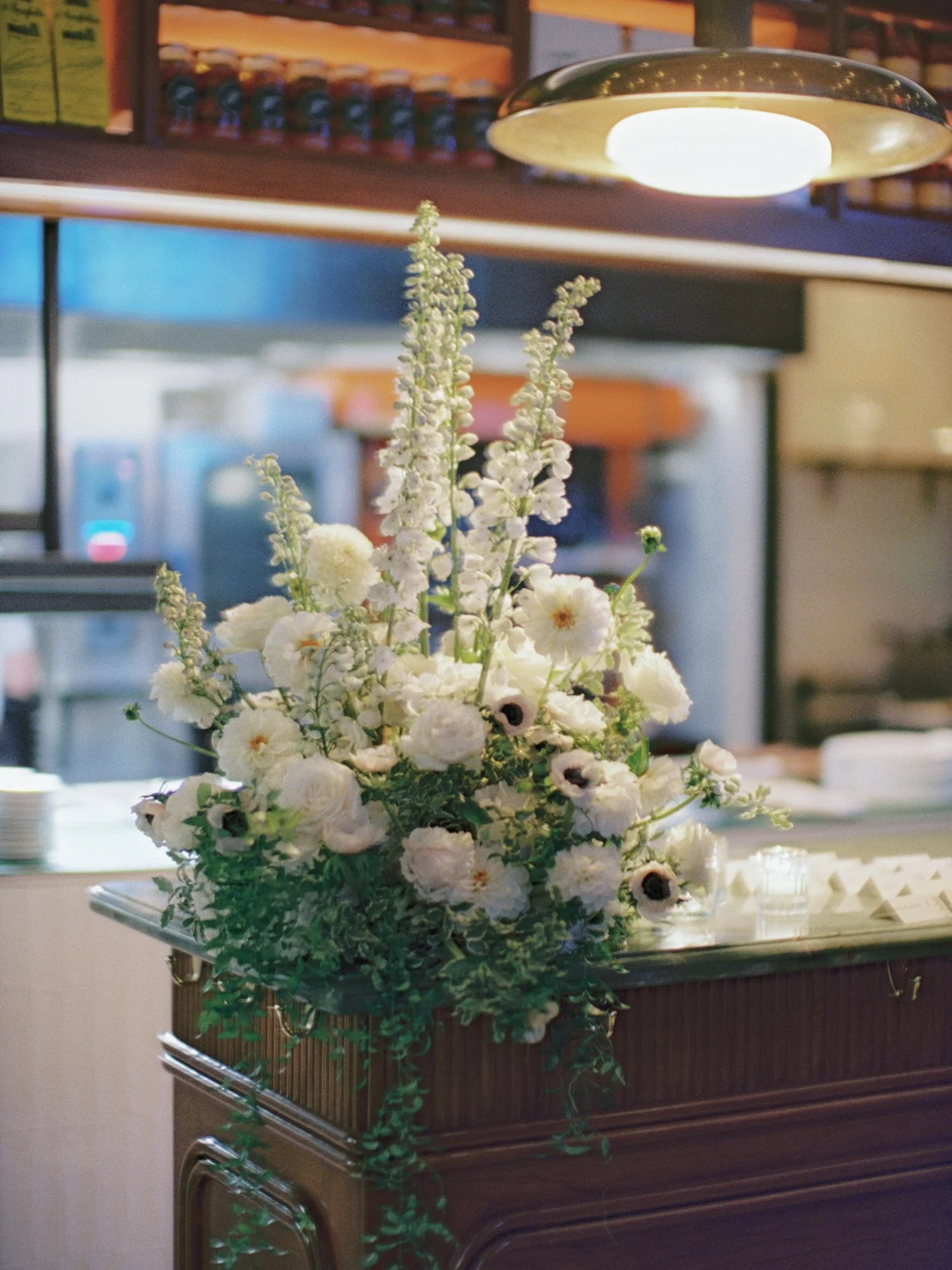 Lush white floral arrangement on the marble bar counter under golden light at Torrisi in Manhattan, photographed by Jenny Fu.