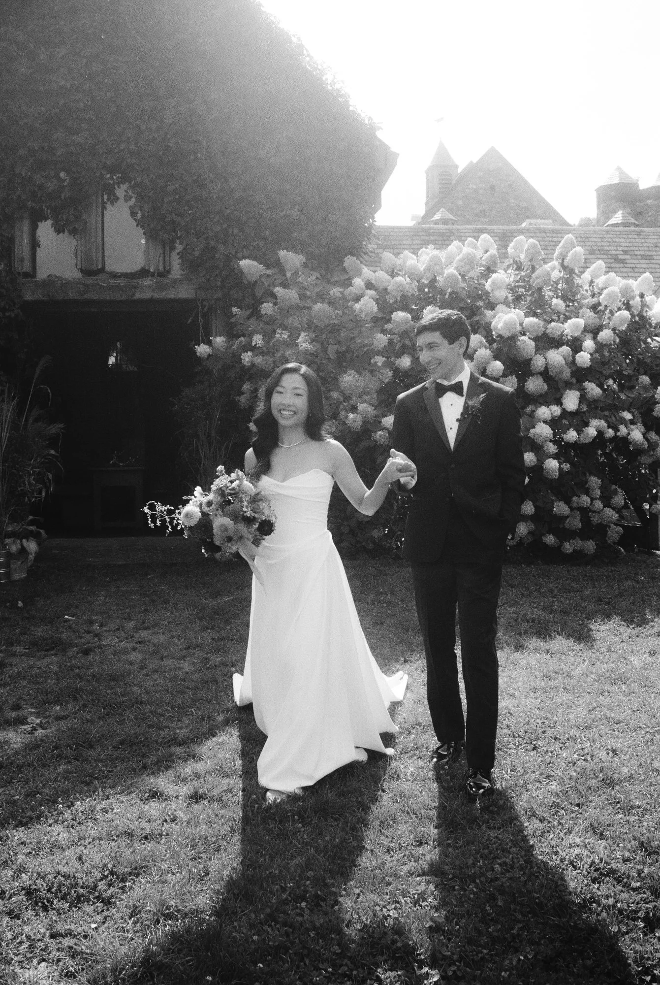Newlyweds walking hand in hand across the lawn beside the hydrangeas in black and white at Blue Hill at Stone Barns, photographed by Jenny Fu.