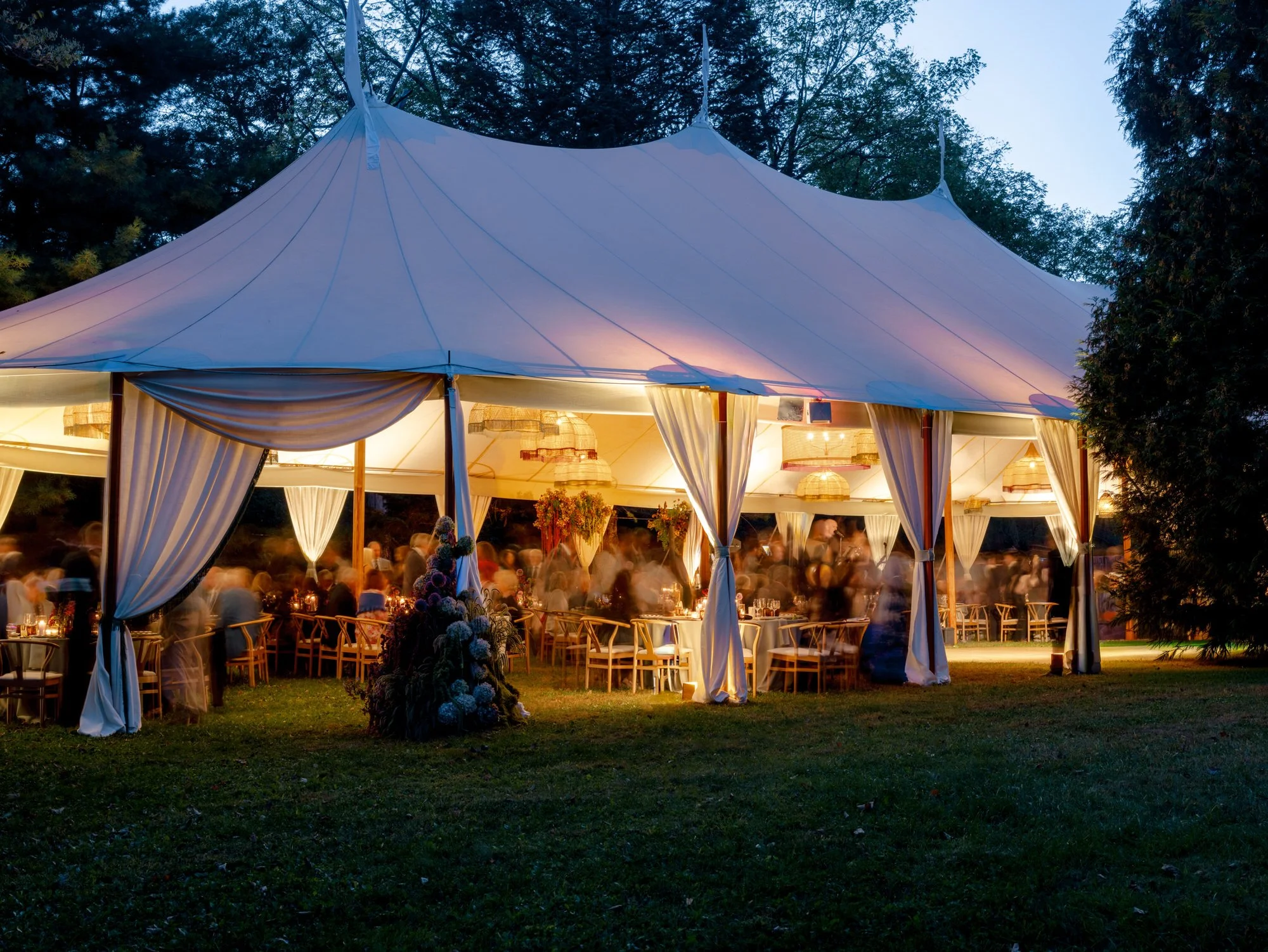 Tented reception glowing at dusk with guests and floral installations visible inside at Troutbeck in Amenia, New York, photographed by Jenny Fu.