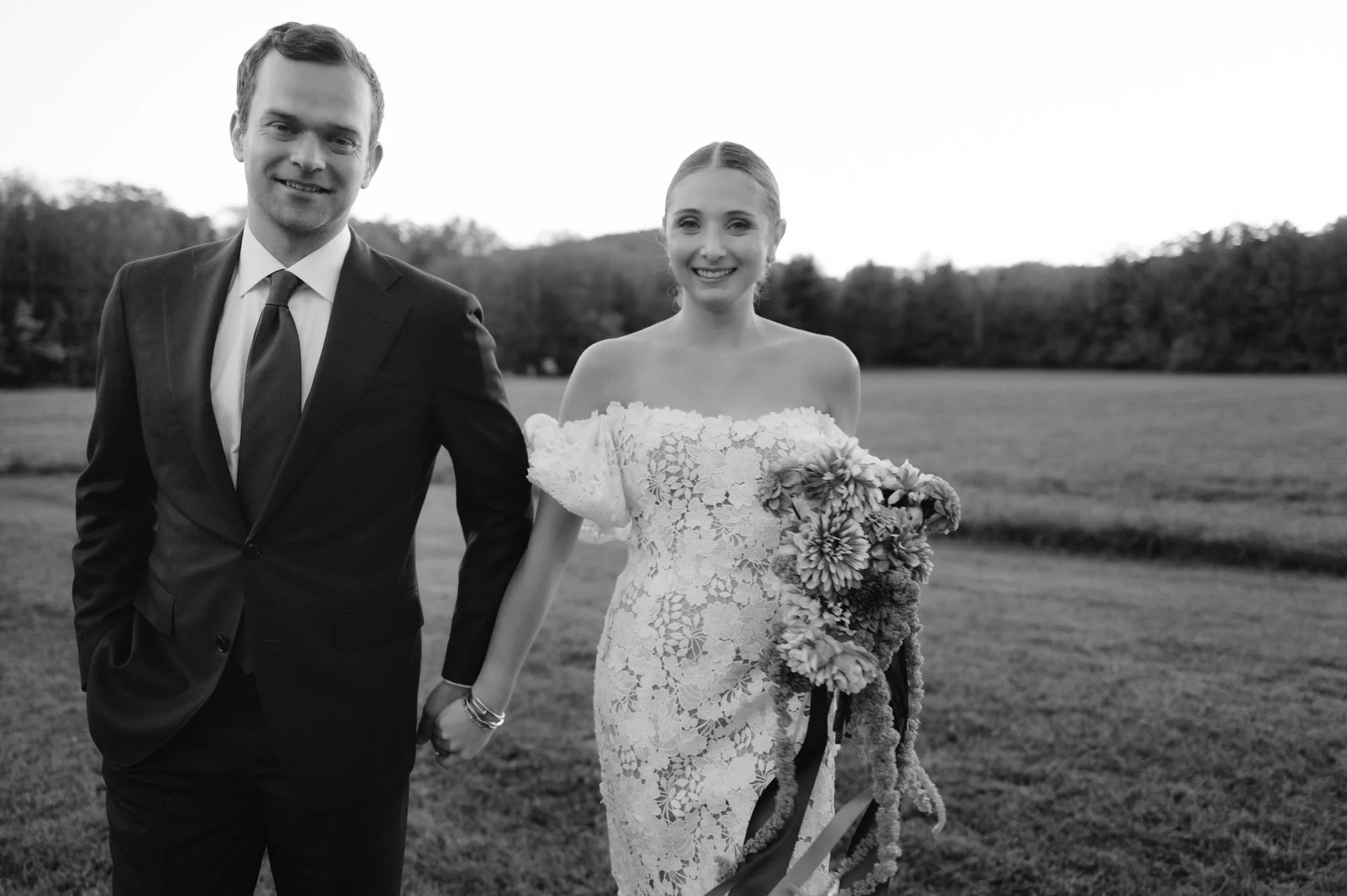 Bride and groom walking hand in hand across a meadow at Troutbeck in Amenia, New York, photographed by Jenny Fu.