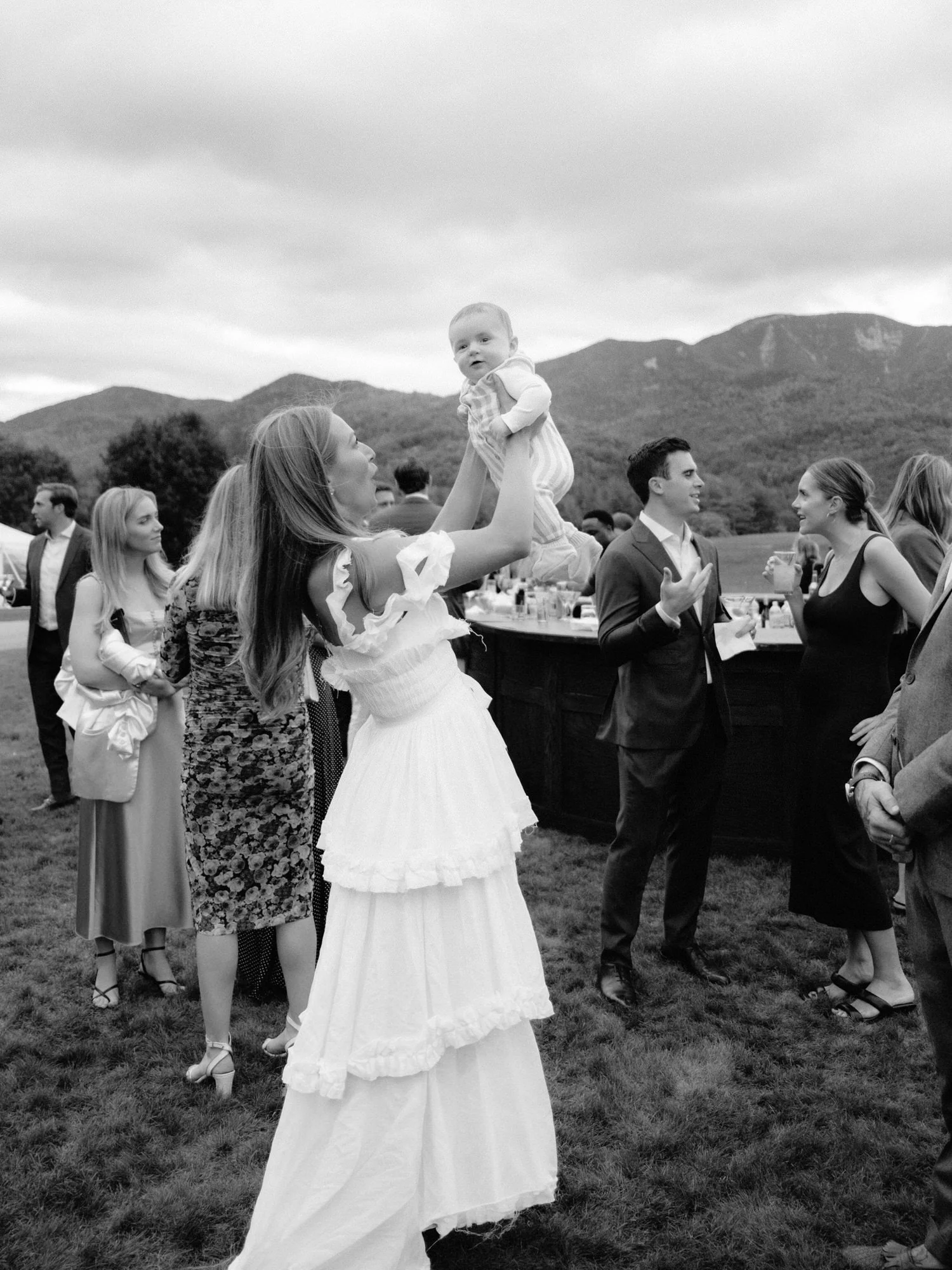 Bride Olivia holding a baby during welcome party rehearsal party cockatil hour at the Ausable Club in the Adirondacks
