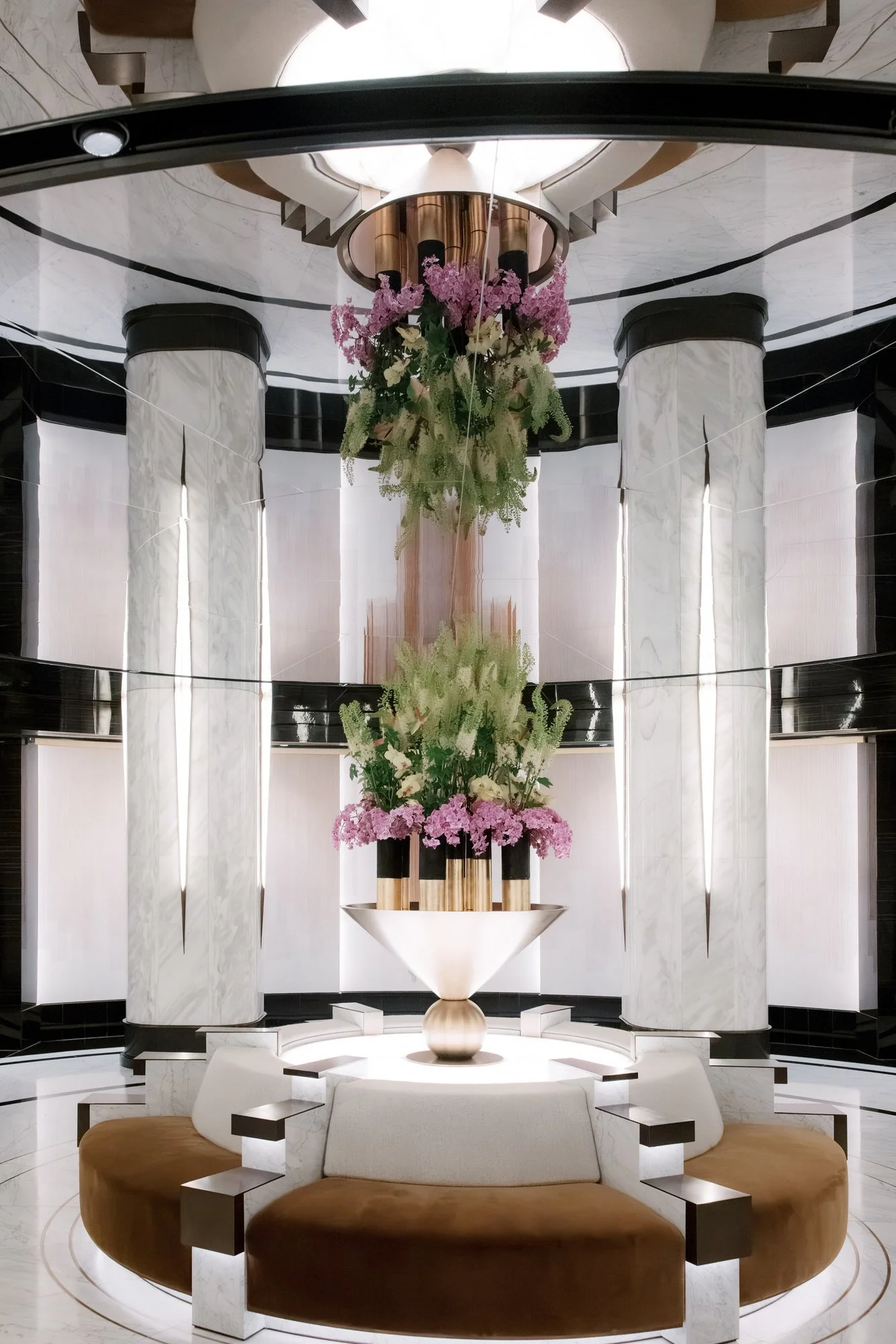 Marble columns, purple florals and a round banquette in a rotunda at the Waldorf Astoria New York, photographed by Jenny Fu.