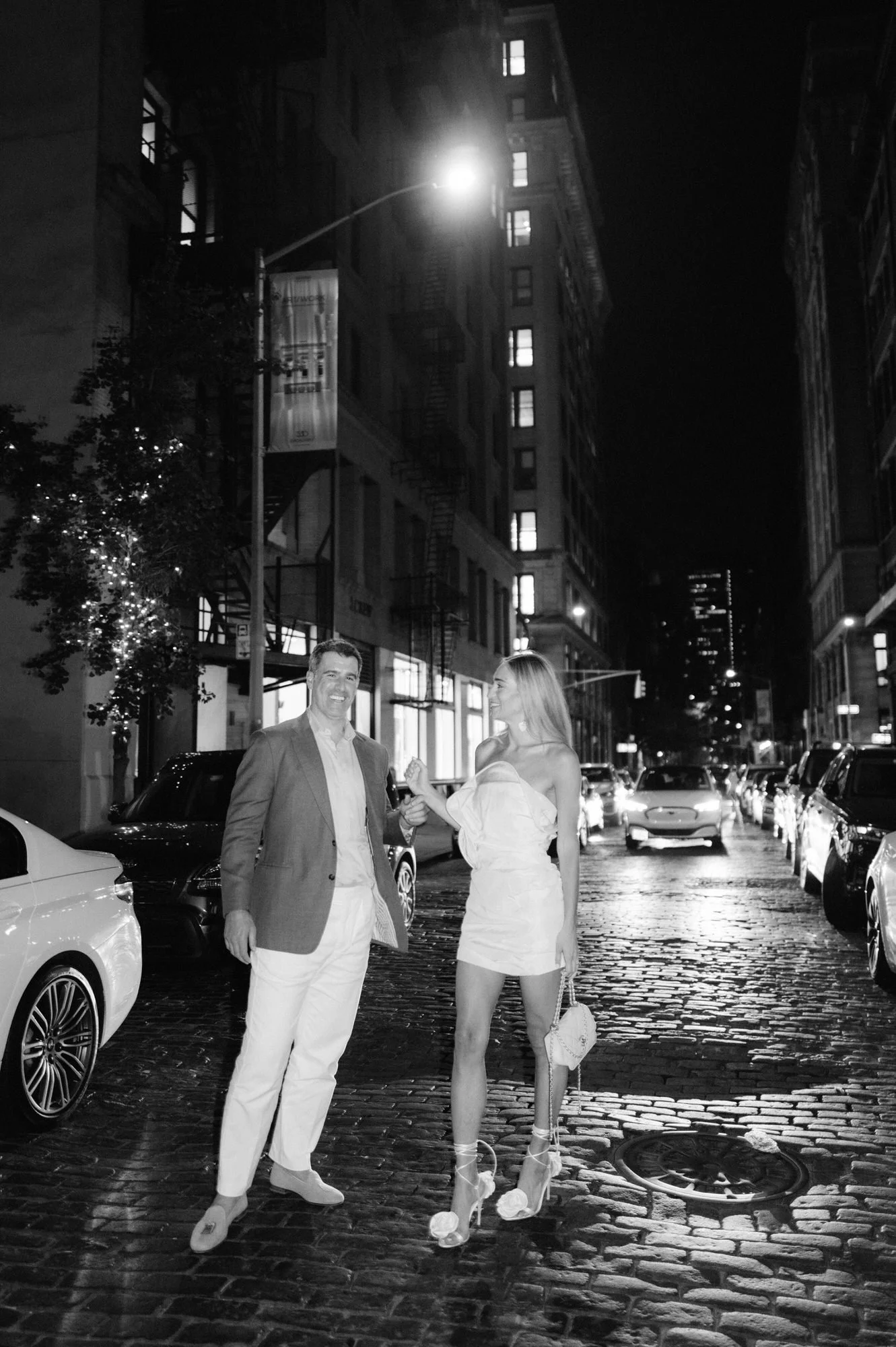 Bride and groom walking hand in hand down a cobblestone street in Soho under city lights, photographed by Jenny Fu.