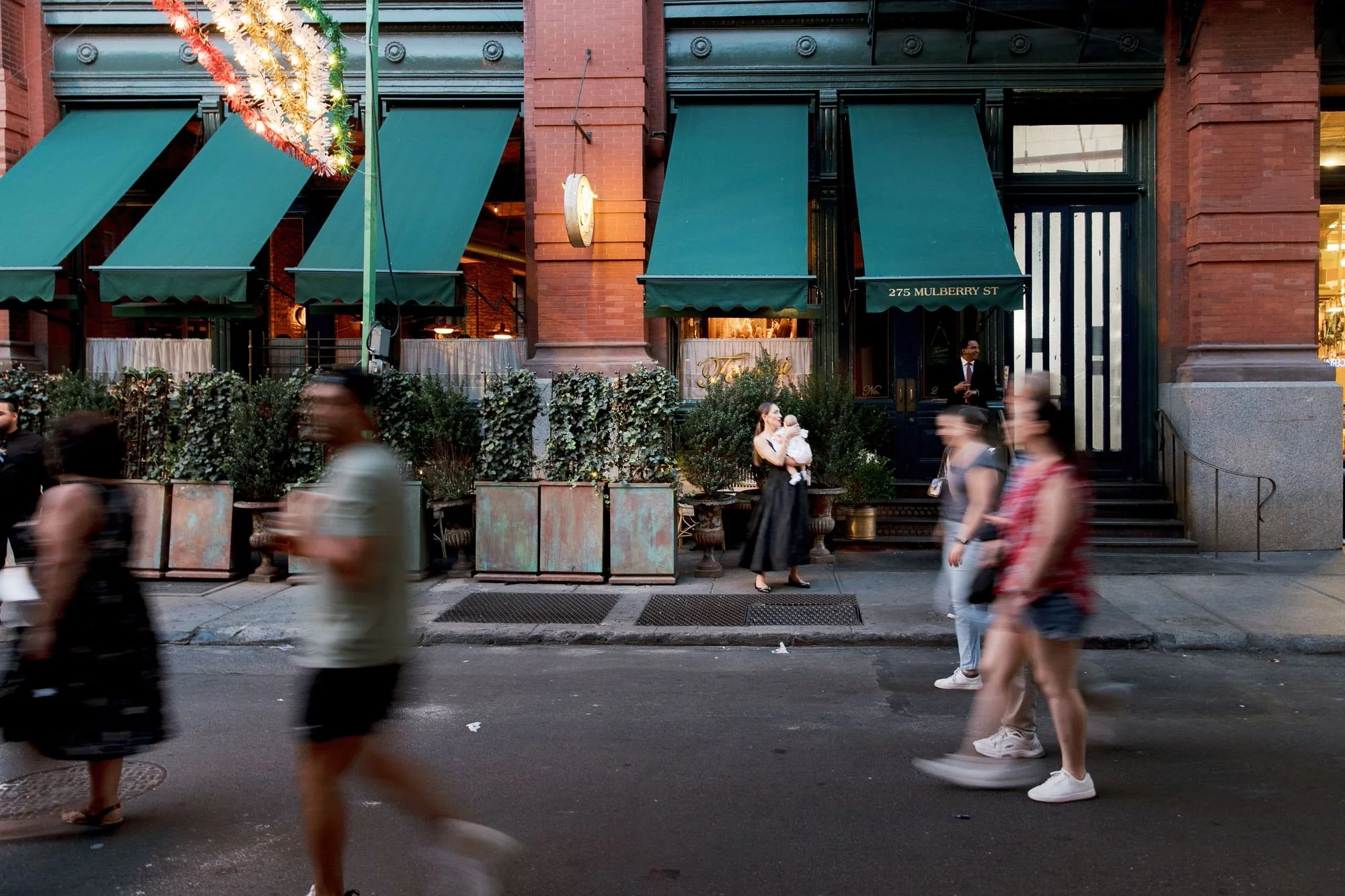 Exterior view of Torrisi on Mulberry Street with its signature green awning and warm evening glow, photographed by Jenny Fu.