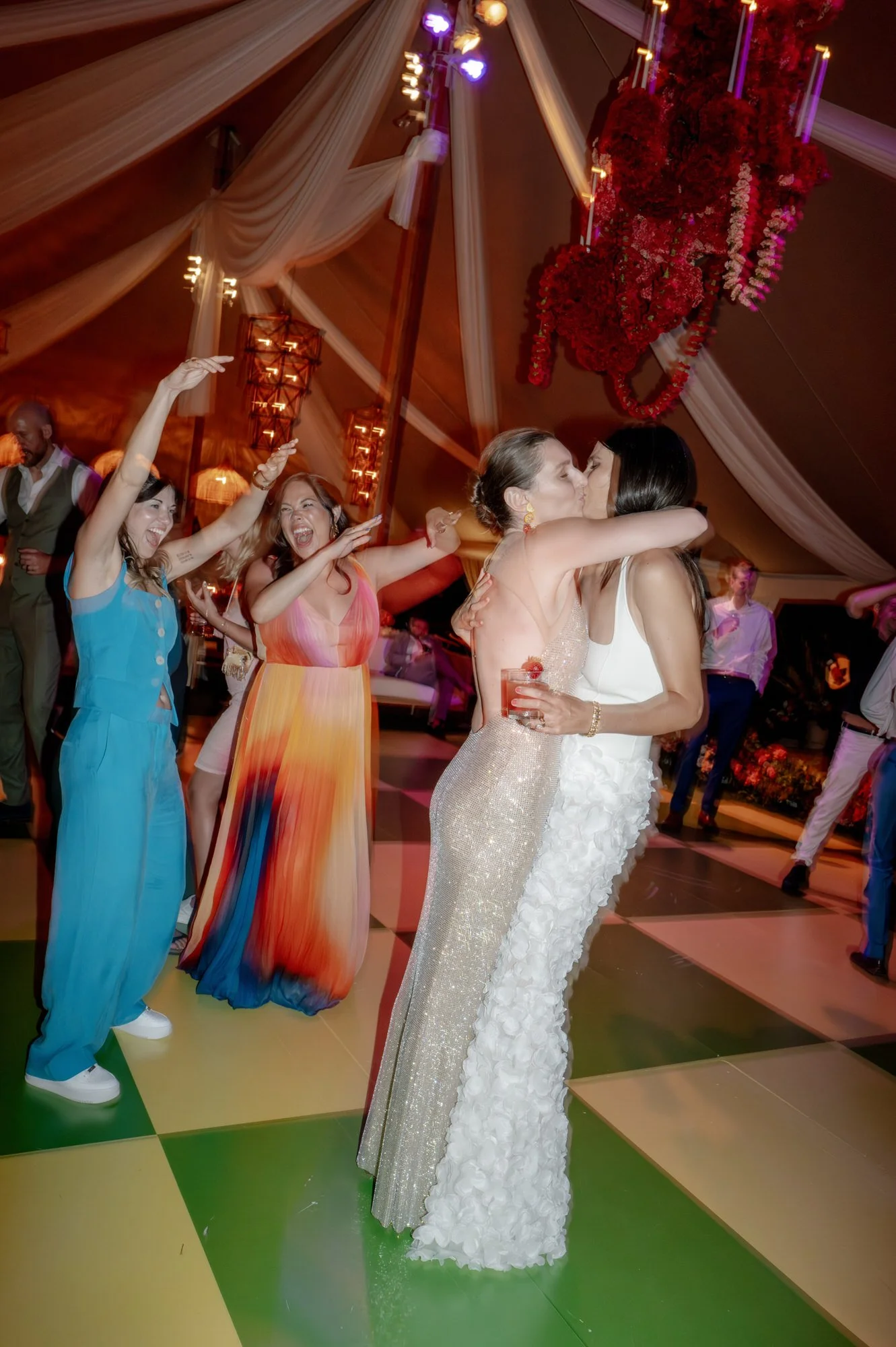 Two brides sharing a kiss on the colorful checkered dance floor beneath a red floral chandelier at Valley Rock Inn in Sloatsburg, photographed by Jenny Fu.