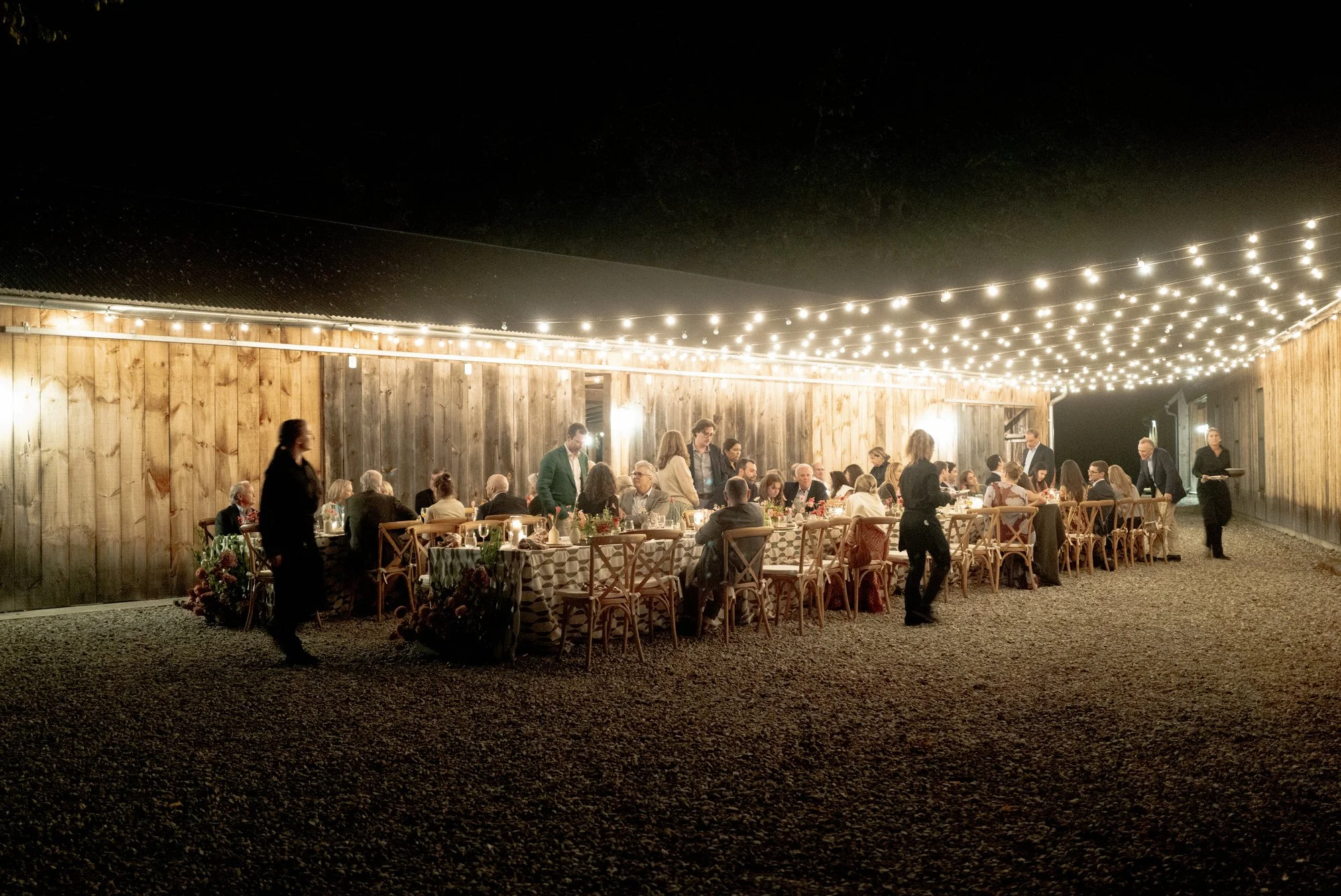 Evening overview of the outdoor dinner party lit by bistro lights in the courtyard at Troutbeck in Amenia, photographed by Jenny Fu.