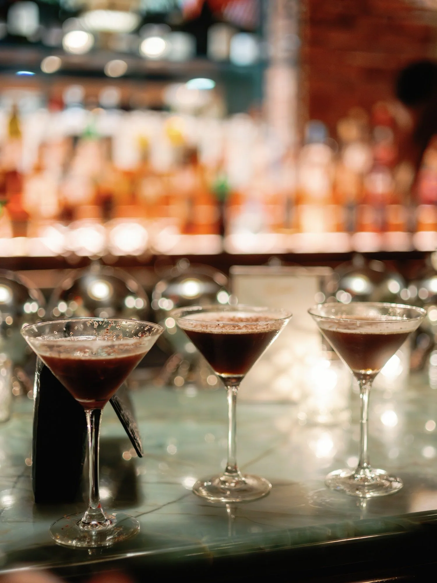 Three espresso martinis glistening under bar light during the wedding reception at Torrisi in Manhattan, photographed by Jenny Fu.
