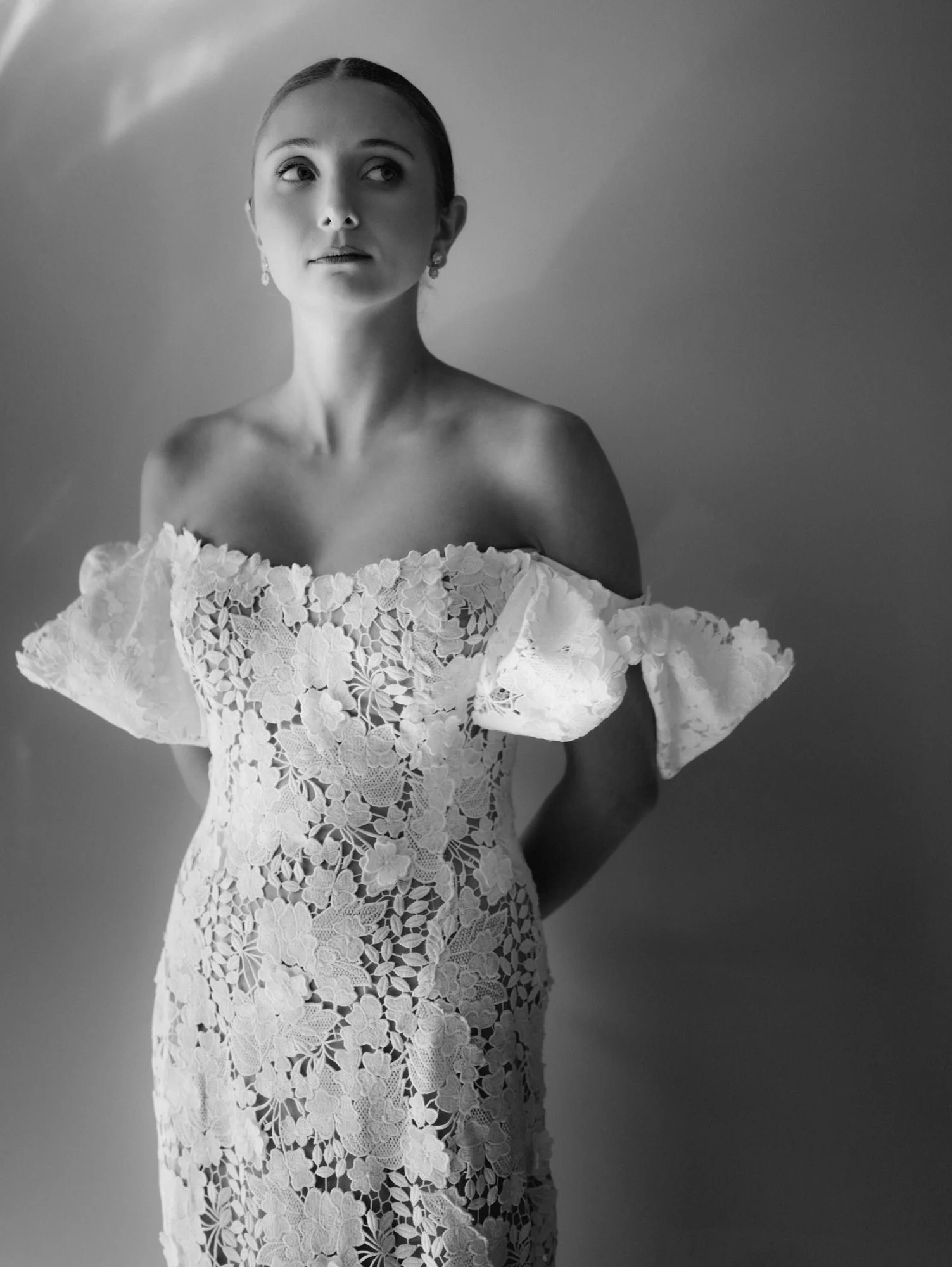 Detail of bride adjusting her off-the-shoulder lace gown in soft window light at Troutbeck in Amenia, photographed by Jenny Fu.