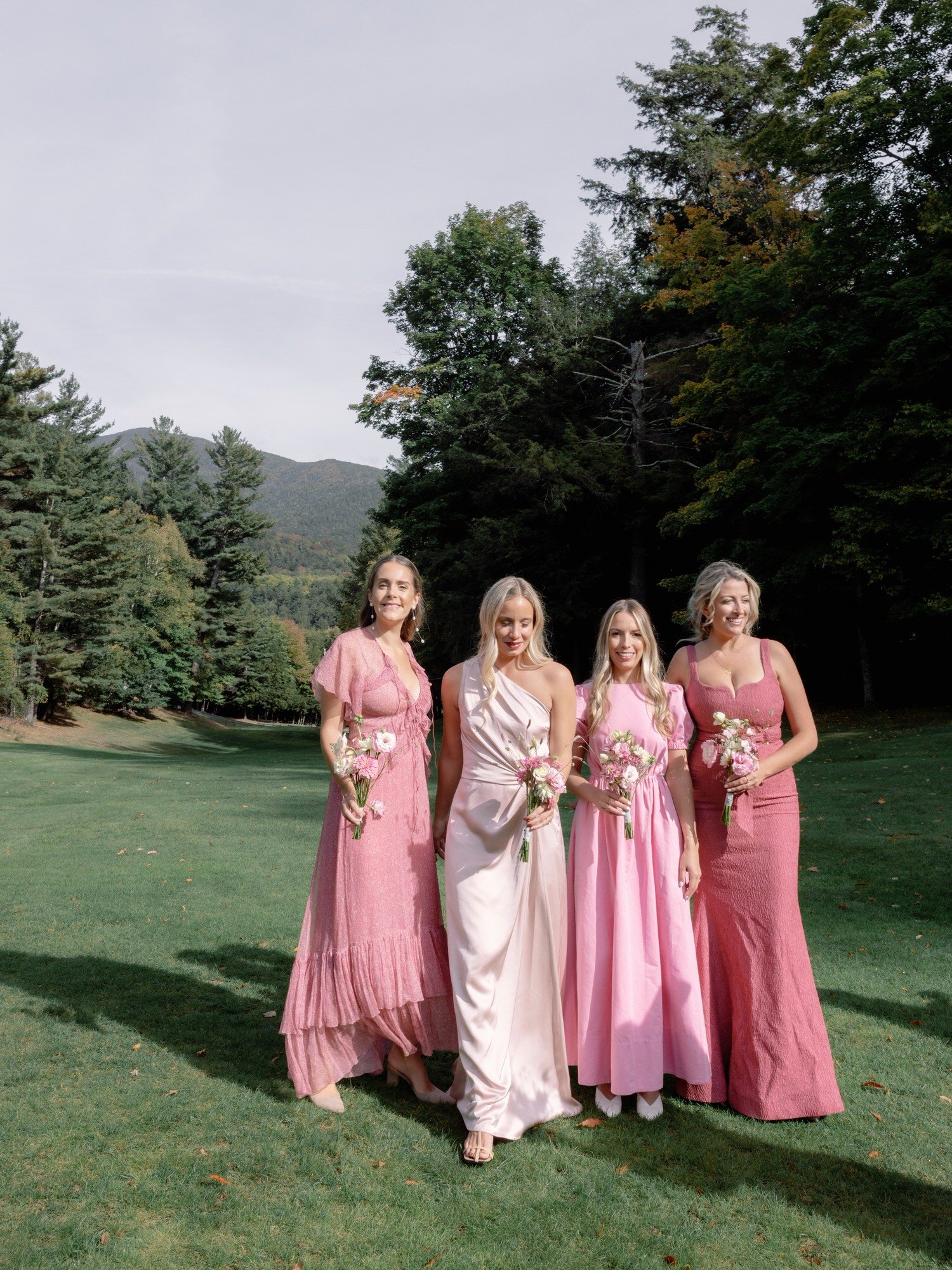 Bridesmaids in pink gowns posing together on the lawn of the Ausable Club in the Adirondacks