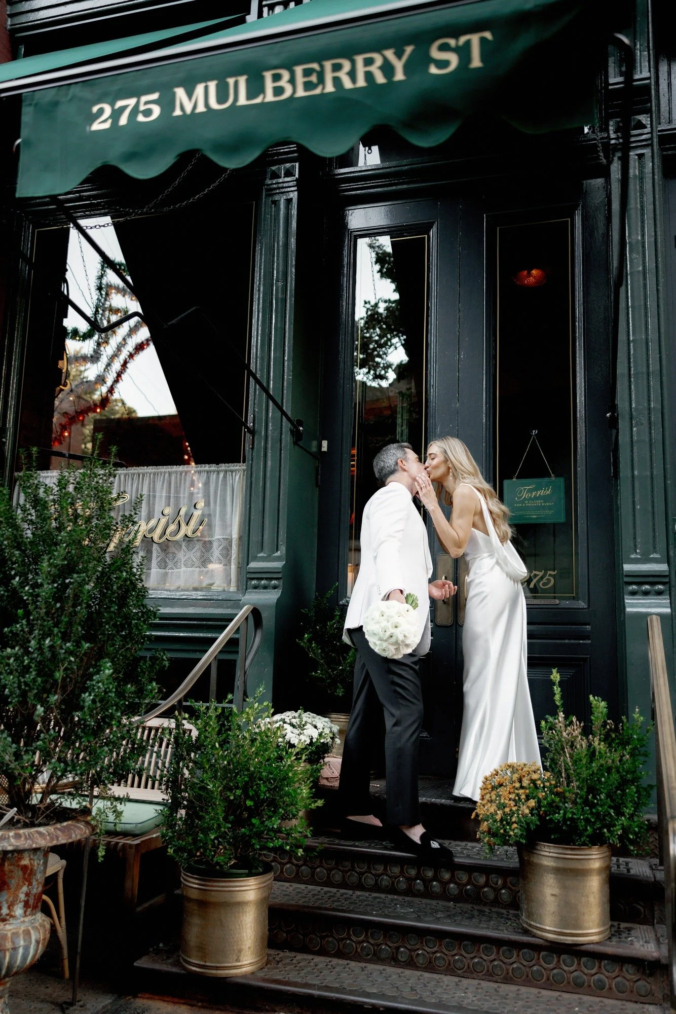 Bride and groom sharing a kiss on the steps beneath the green awning of Torrisi in Manhattan, photographed by Jenny Fu.