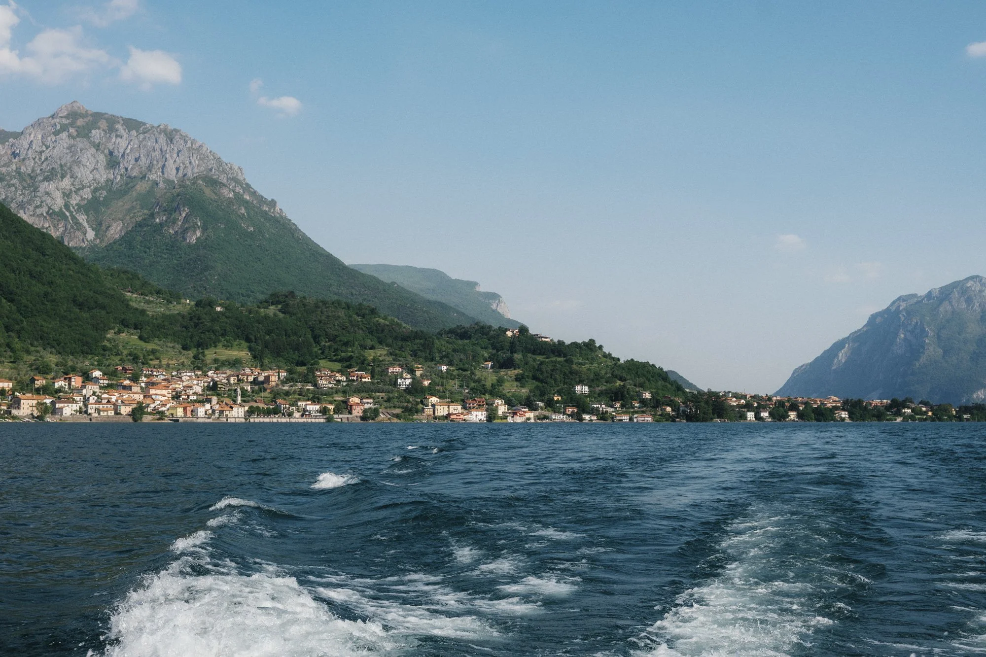 Lakeside village and mountains seen from the wake of a boat on Lake Como, Italy, photographed by Jenny Fu.