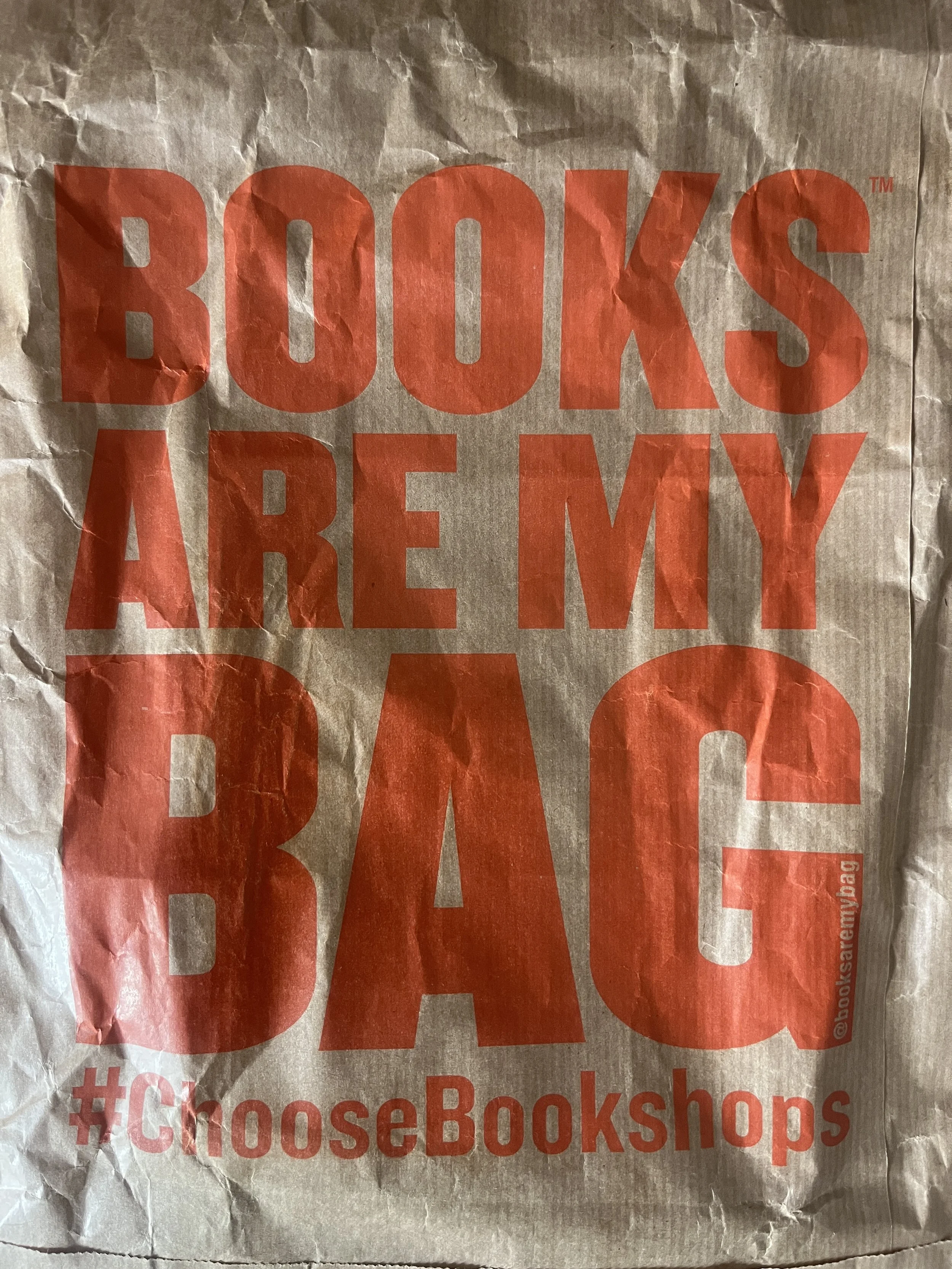 Crinkled brown paper bag with red text reading "BOOKS ARE MY BAG" and a hashtag #ChooseBookshops.