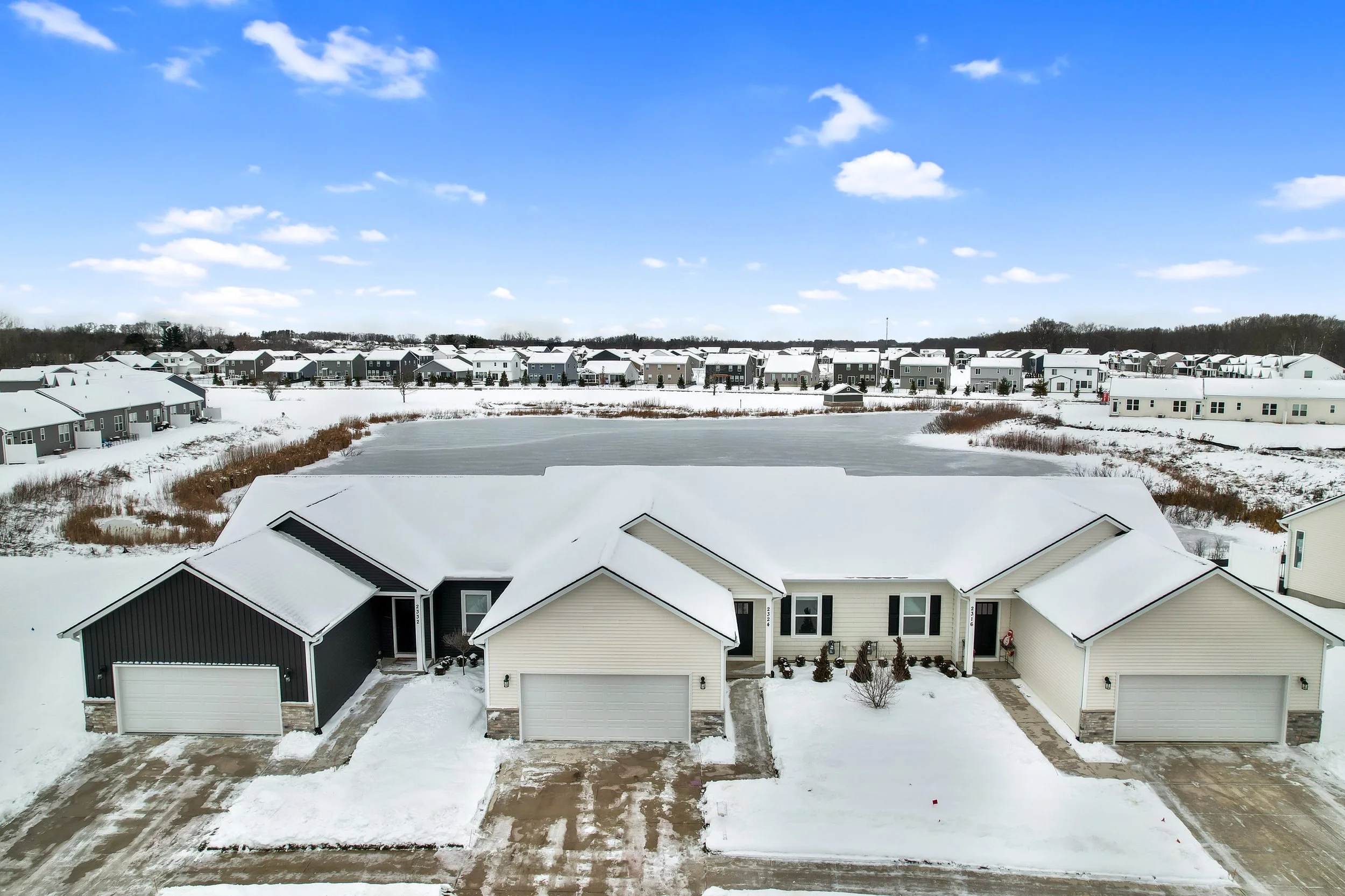 Ranch style condominium in howell michigan on a pond. Linnen white and ironside gray vynil siding with black shutters. snowy shoveled driveways.