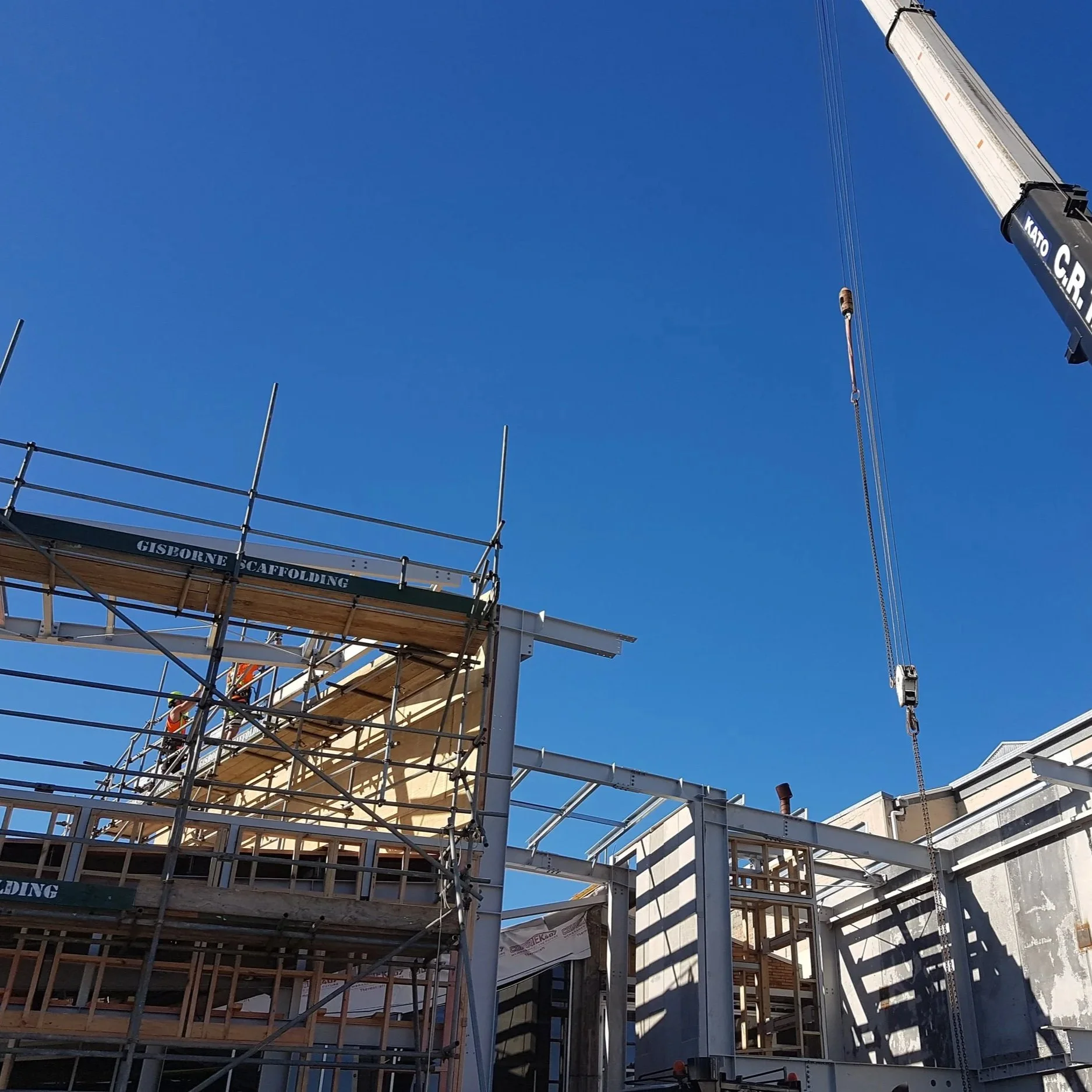 Construction site with scaffolding and a crane, building framework visible against a clear blue sky.