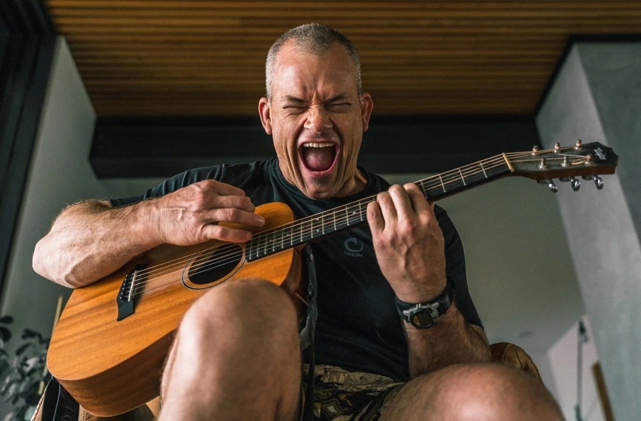 A man passionately playing an acoustic guitar and singing with his eyes closed and mouth wide open.