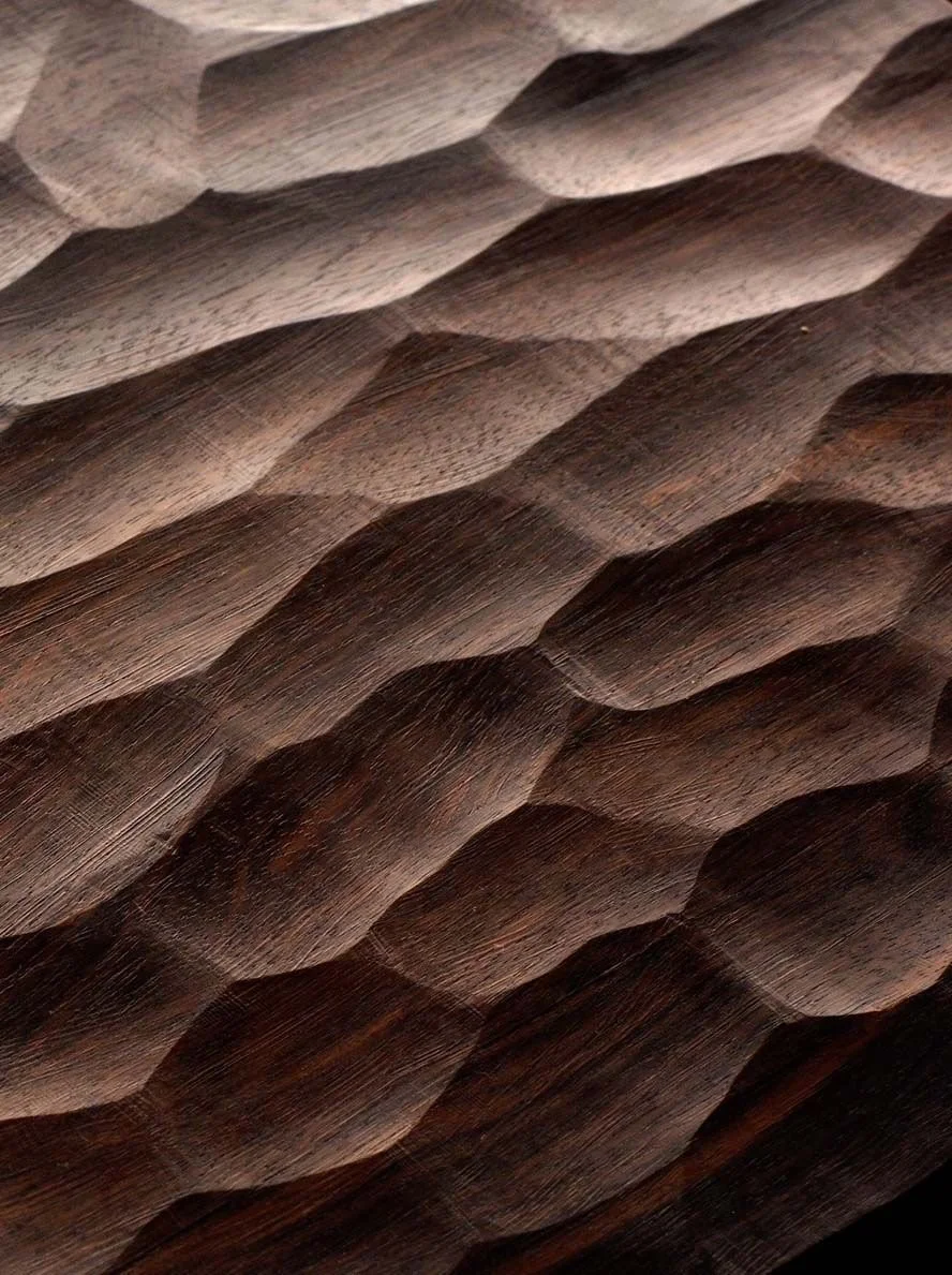 Close-up of a textured wooden surface with a pattern of overlapping, rounded, and carved shapes.