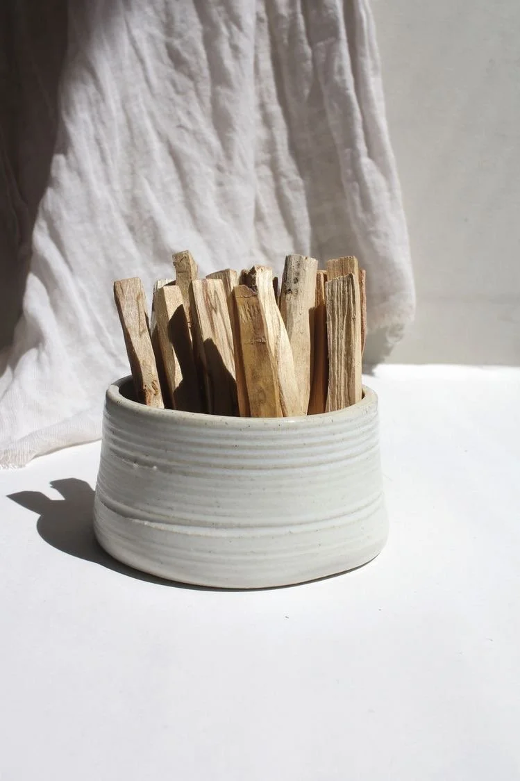 Wooden sticks in a white ceramic bowl on a white surface with a white cloth in the background.