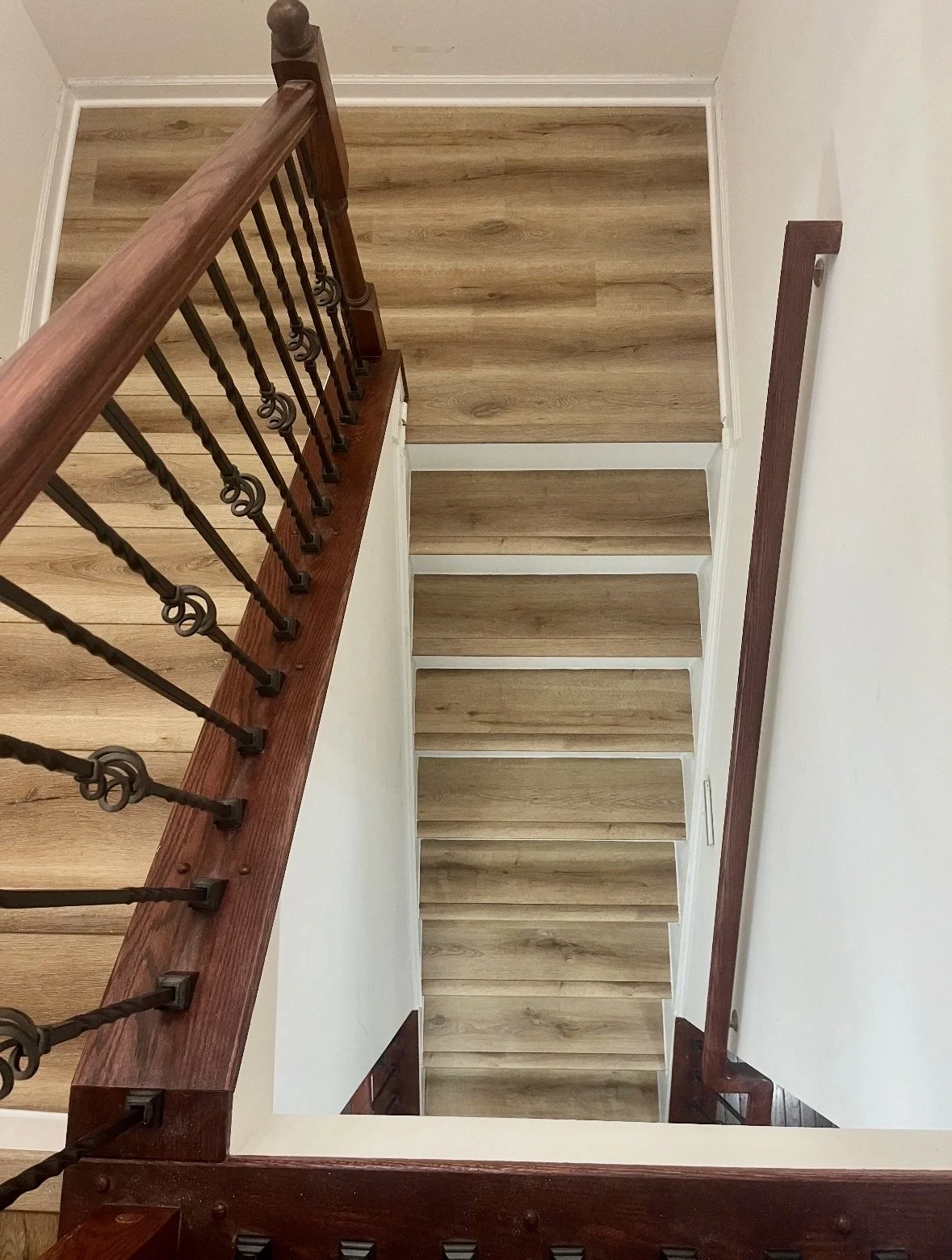 DMV DC, Maryland, Virginia flooring and carpet home repair, View looking down a staircase with wooden steps, a wooden handrail, and decorative wrought iron balusters.