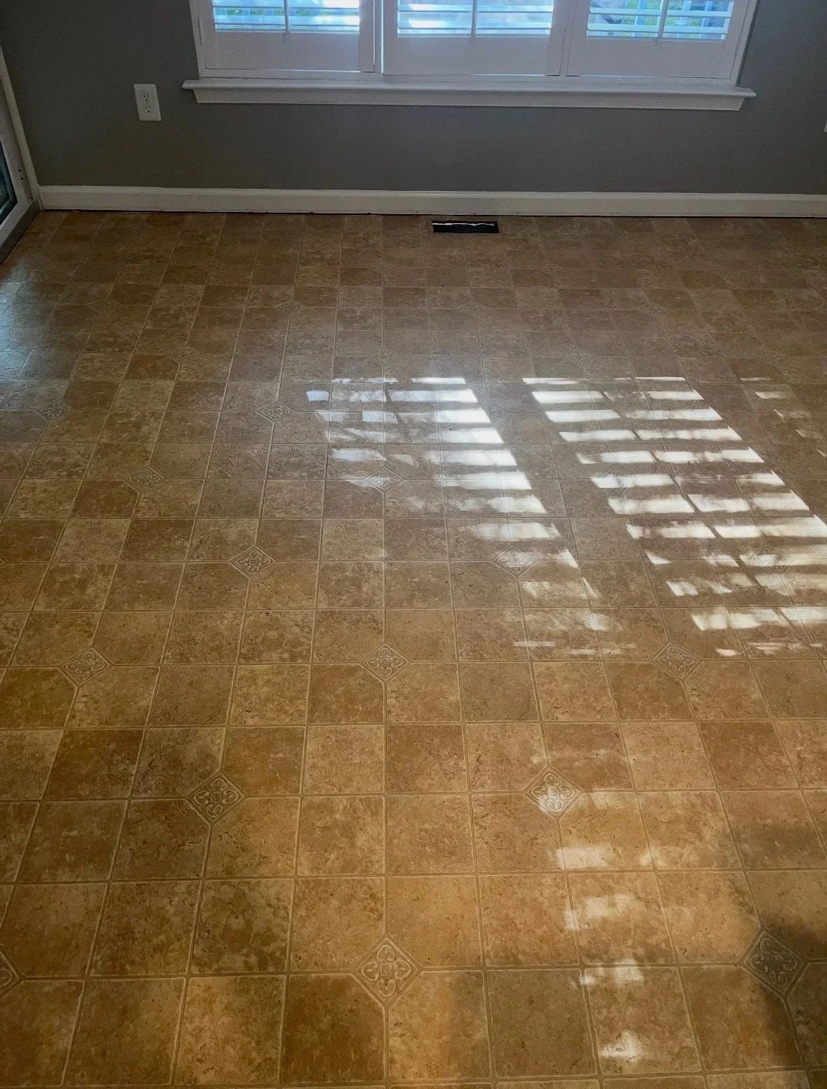 DMV DC, Maryland, Virginia flooring and carpet home repair, Empty room with brown tiled floor, a window with blinds casting light and shadows, a gray wall, and a vent on the floor.