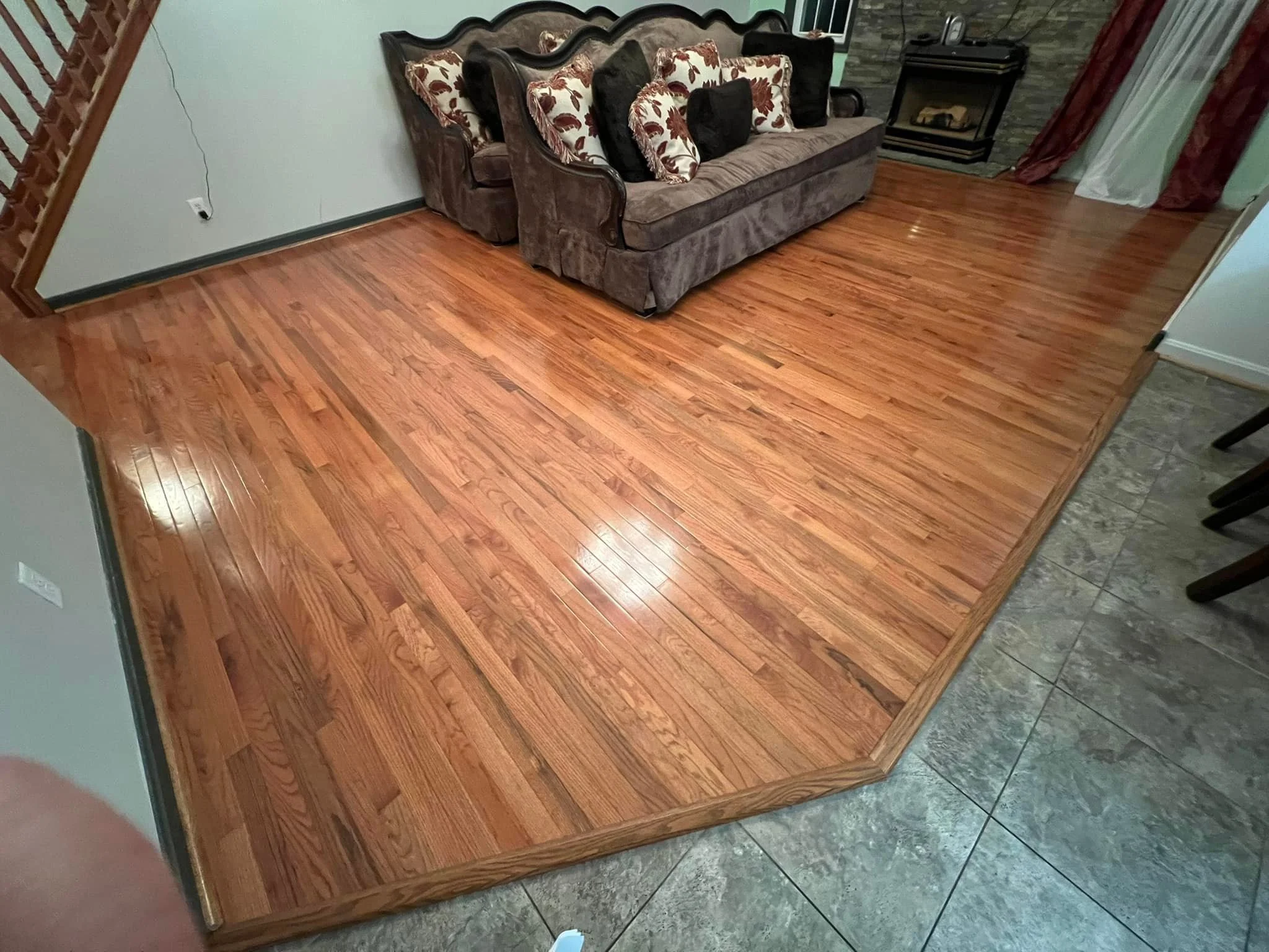 DMV DC, Maryland, Virginia flooring and carpet home repair, Living room with hardwood flooring, a gray upholstered sofa with floral and black throw pillows, a fireplace, and curtains.