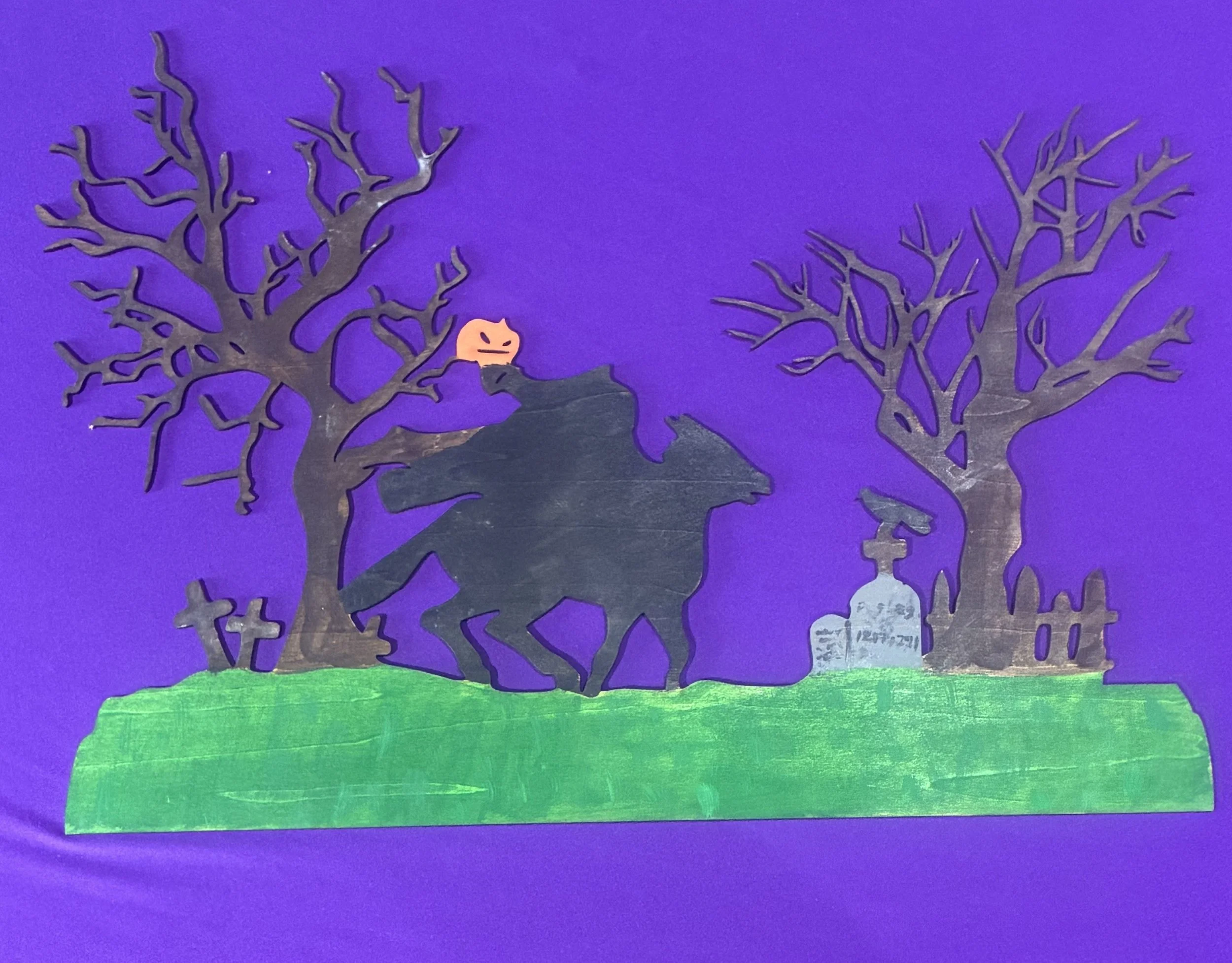 Colorful drawing featuring a dark purple night sky, a bright orange moon with a face, and two leafless trees with twisted branches on either side, standing on a grassy green hill.
