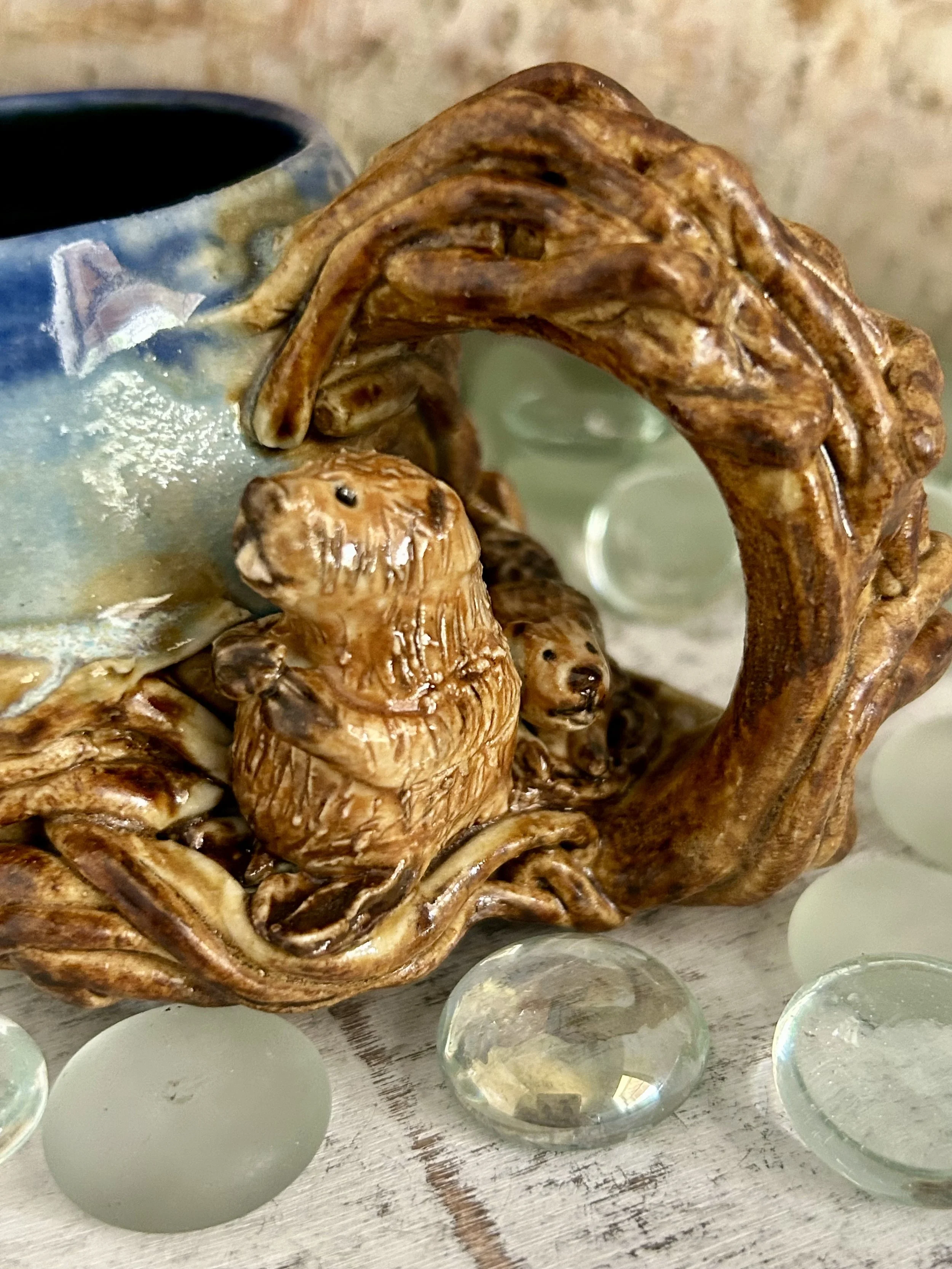 Wooden sculpture of a bear family with a cub inside a naturalistic wooden frame, surrounded by glass pebbles.