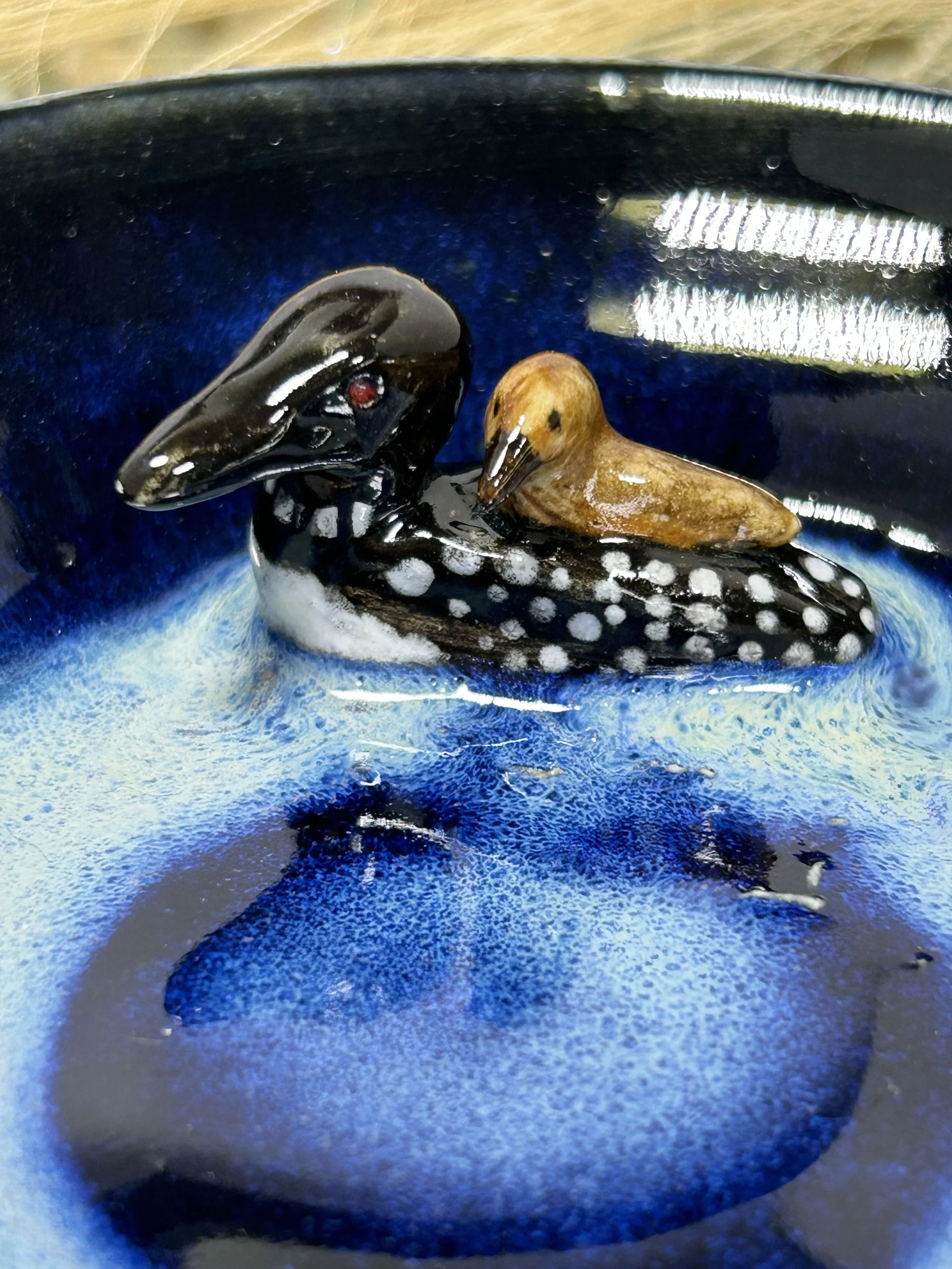 A small decorative sculpture of a black and white dotted fish with a smaller brown bird resting on its back, set against a dark blue background with a reflective surface.