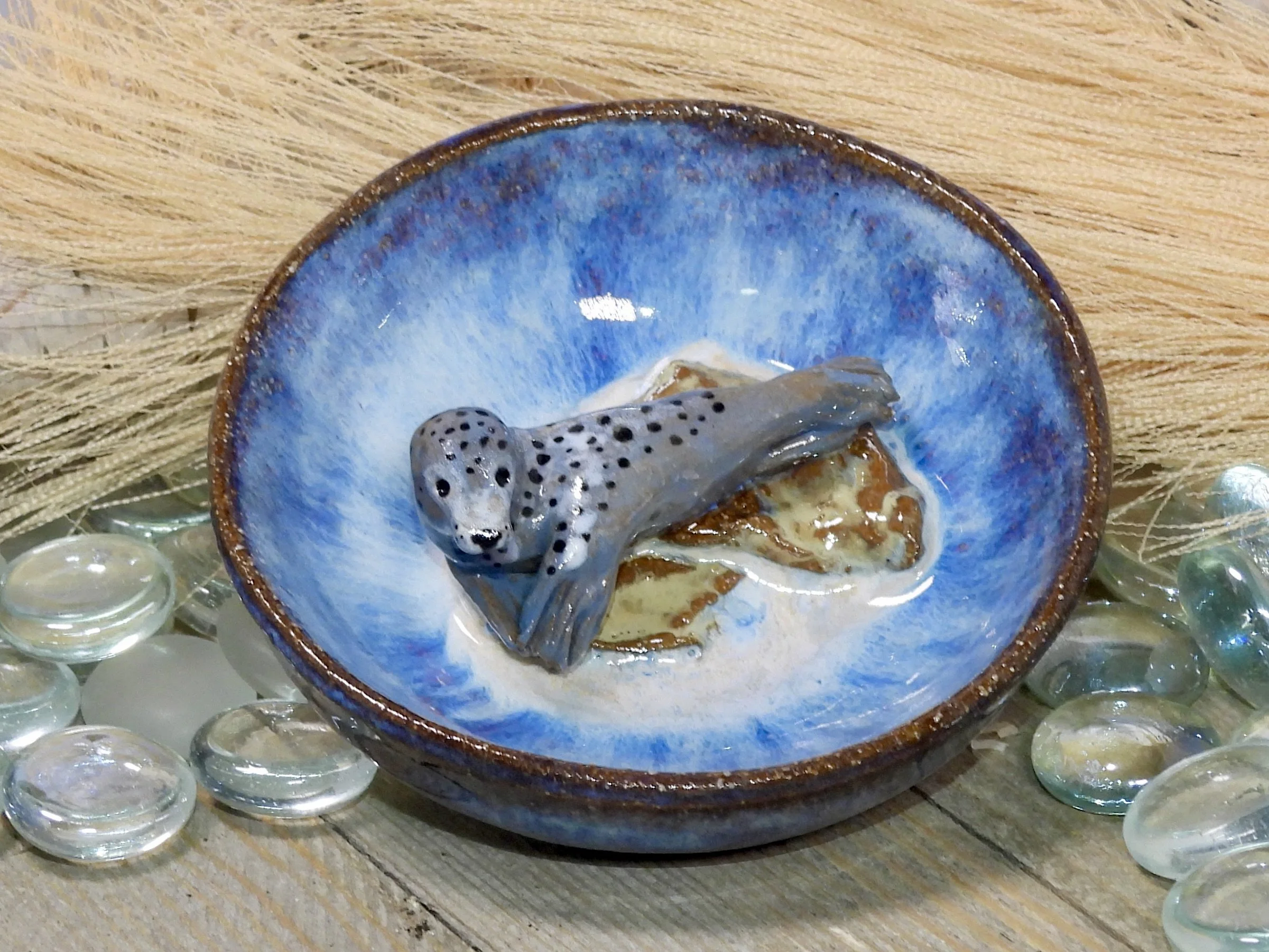 A ceramic bowl with a blue and brown glaze, containing a small, detailed model of a gray leopard lounging on a rock.