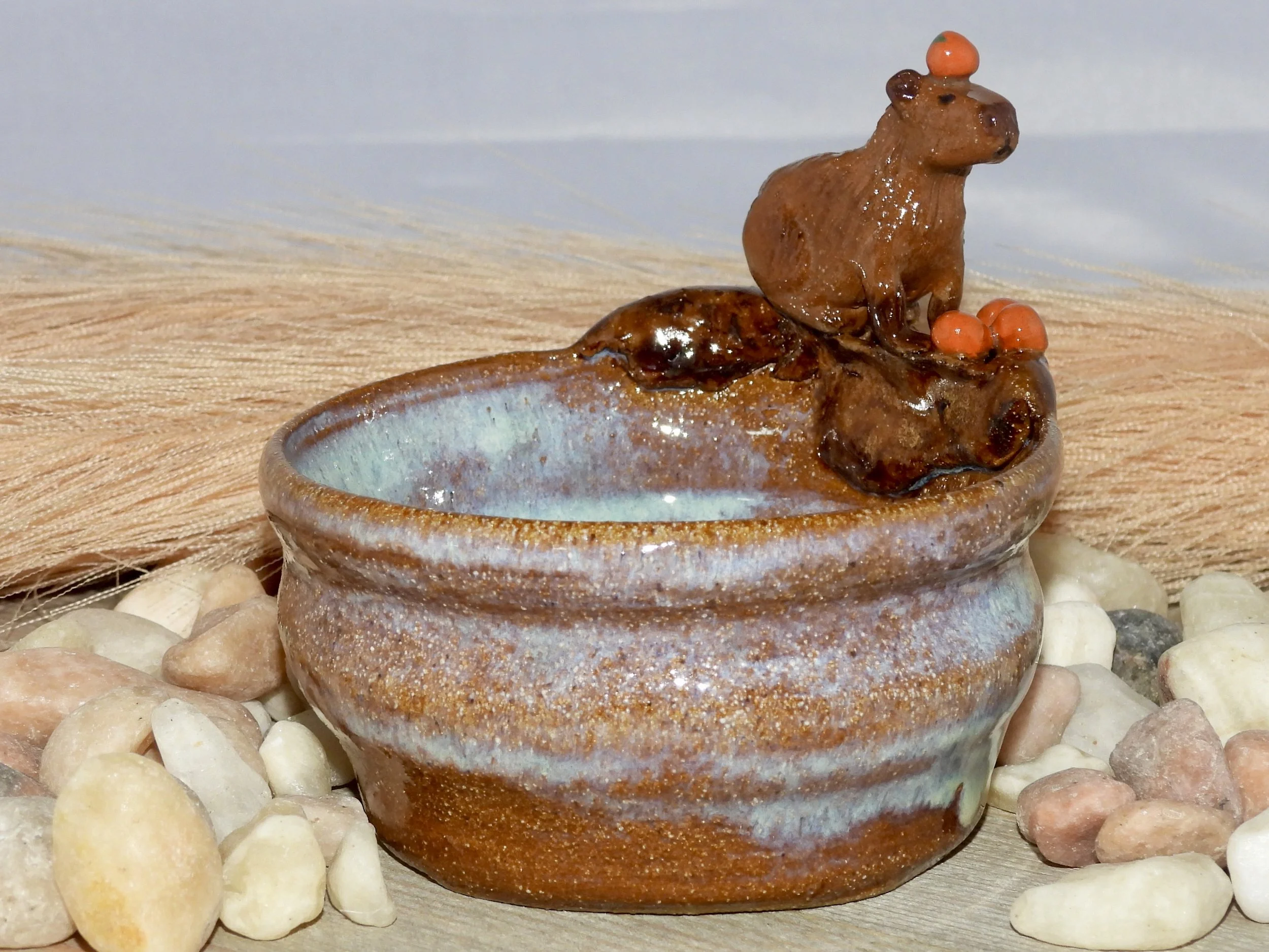 A small decorative ceramic bowl with a moose figurine and orange berries on top, surrounded by pebbles.