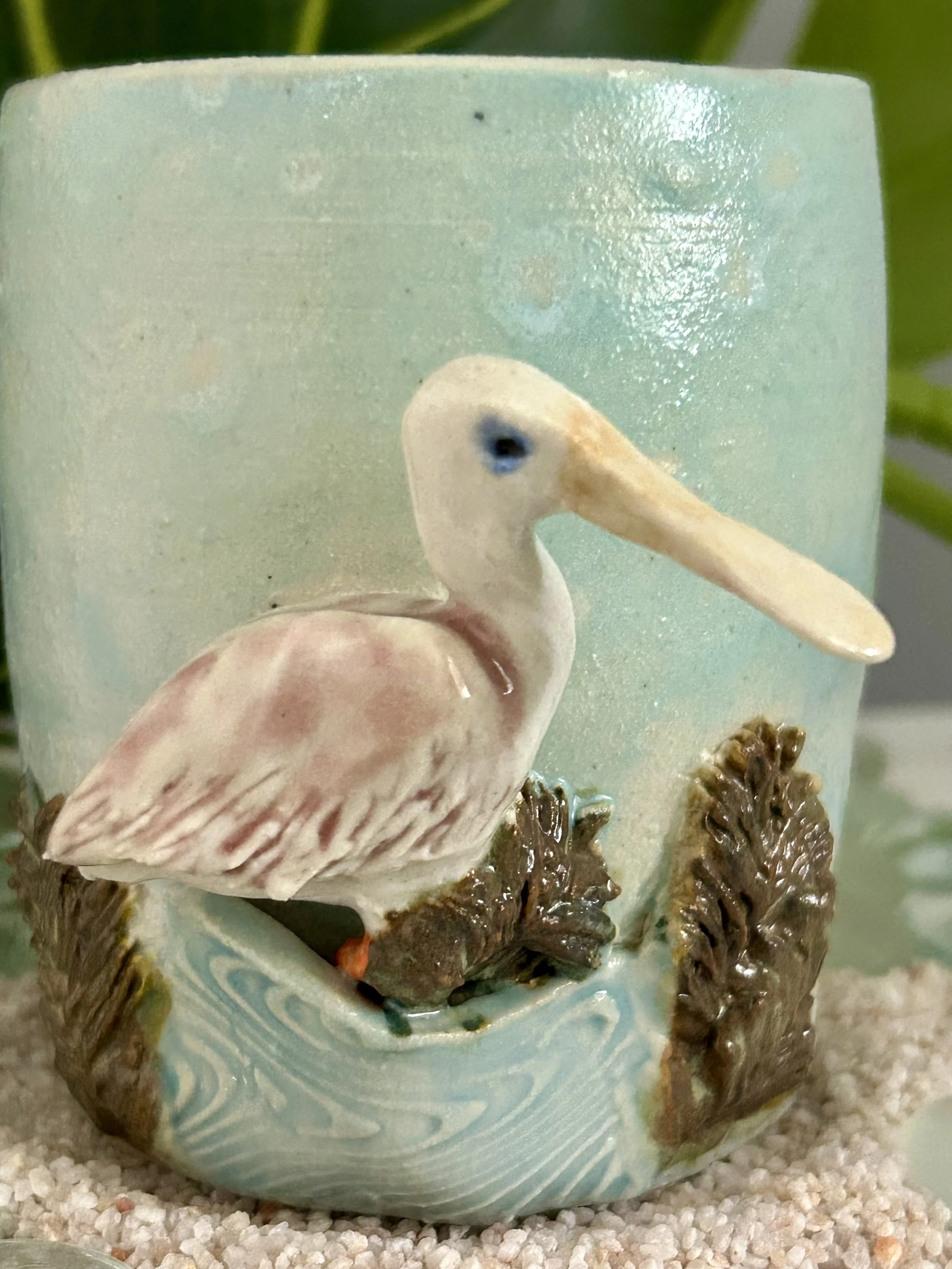 Decorative item featuring a ceramic pelican perched on rocks with water design, in front of a light blue container.