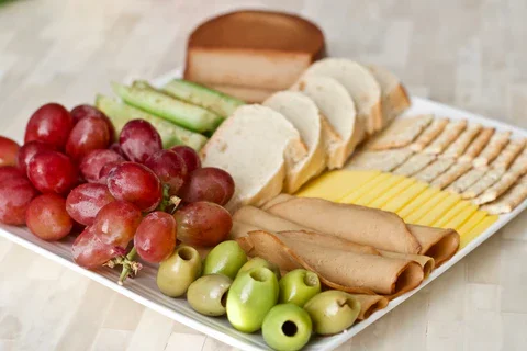 charcuterie plate filled with bread, crackers, vegan cheeses, tofurky slices, grapes and olives