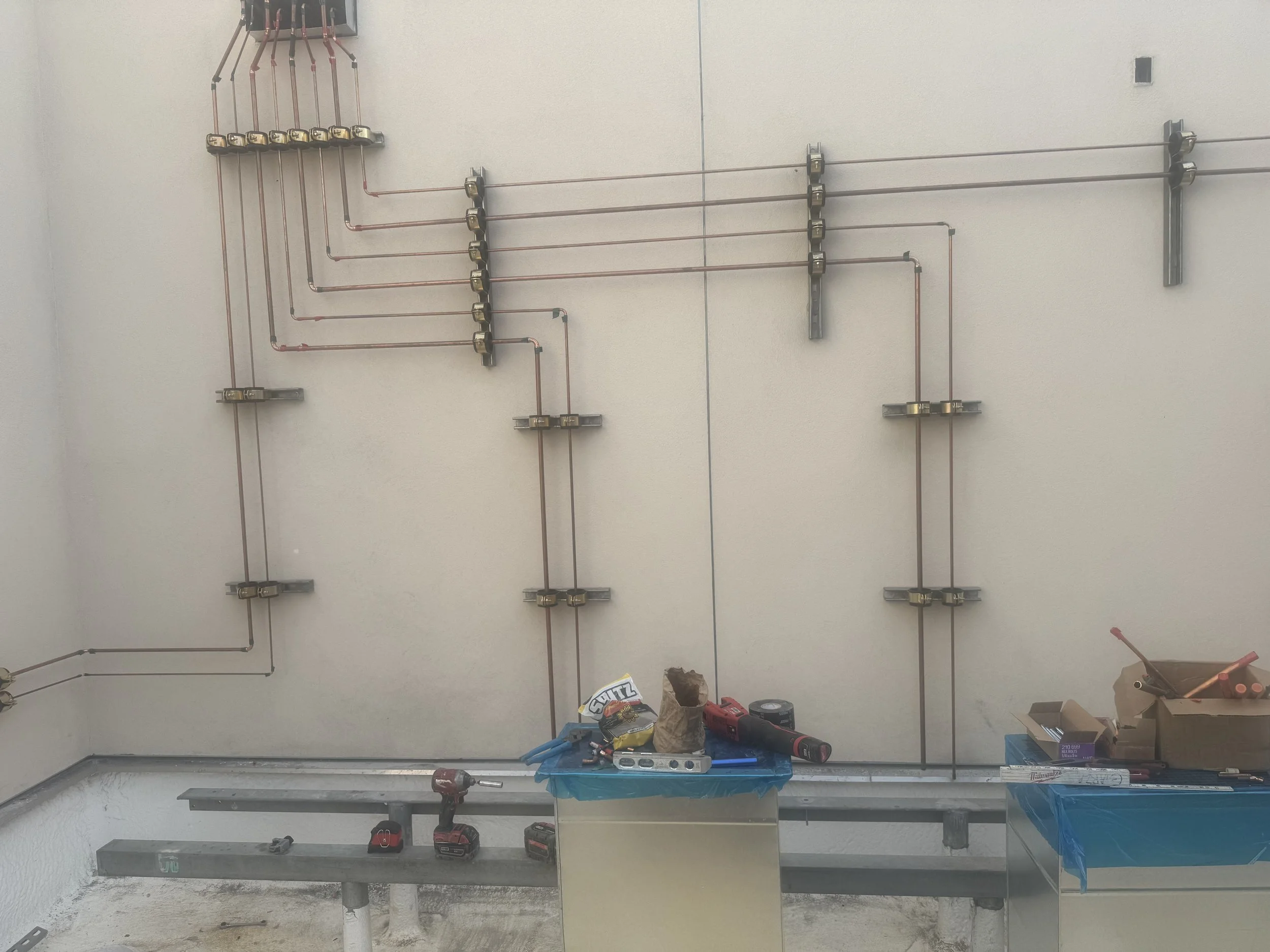 Construction site with exposed copper pipes on a wall, tools, and equipment on the floor and tables.