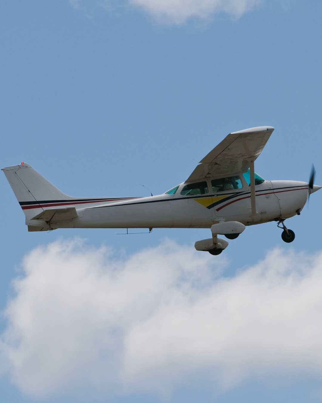Small white plane flying in a partly cloudy sky.