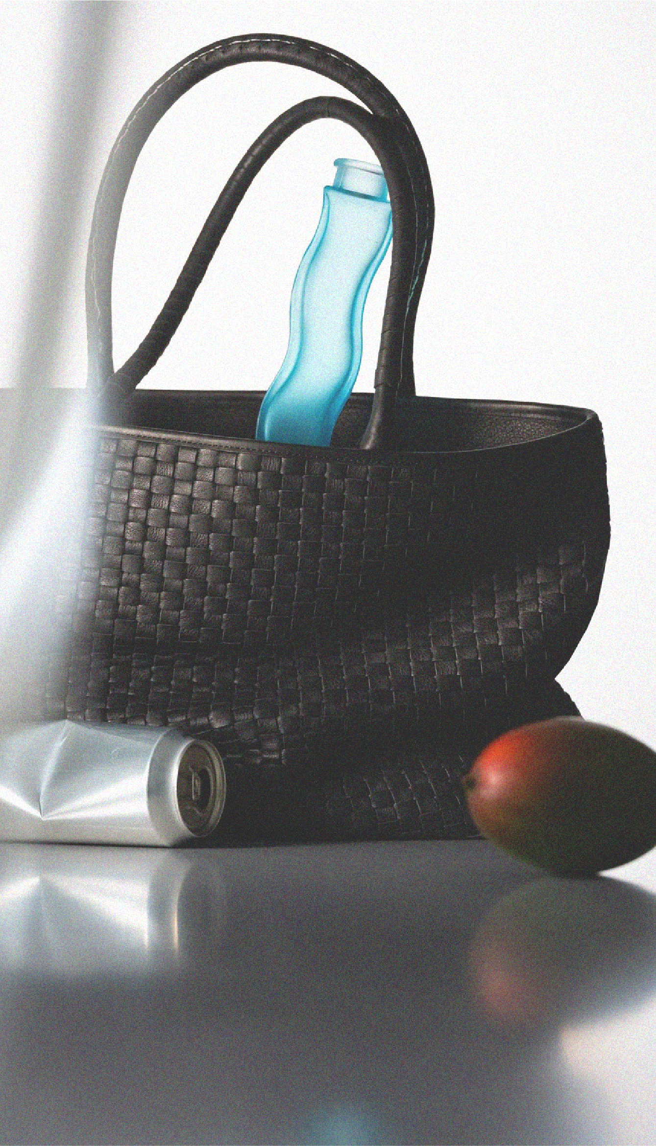 A black woven handbag with a blue plastic water bottle inside, a partially visible aluminum soda can, and a red apple nearby on a reflective silver surface.