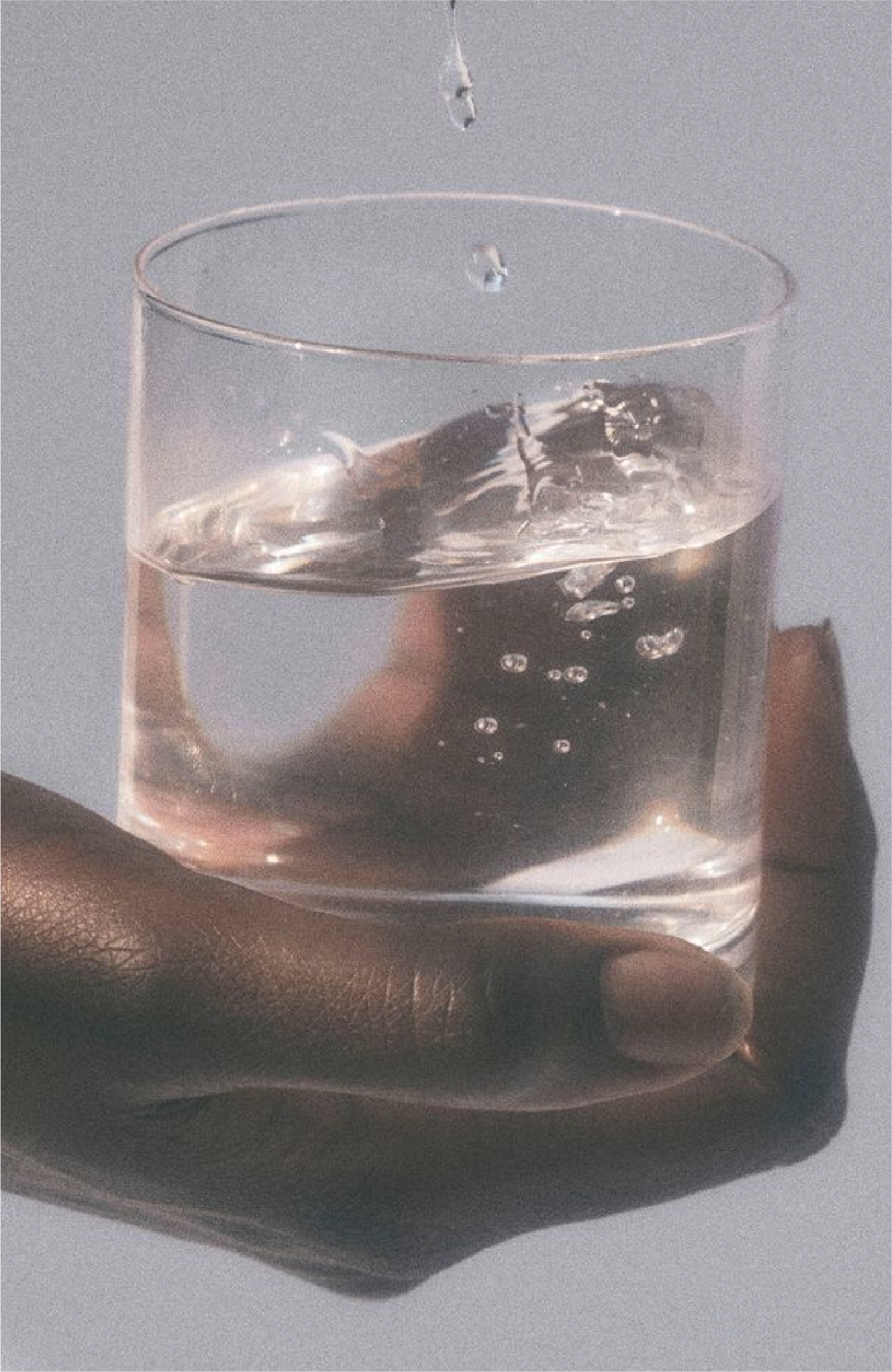 A clear glass of water with ice cubes and bubbles, held by a person's hand.