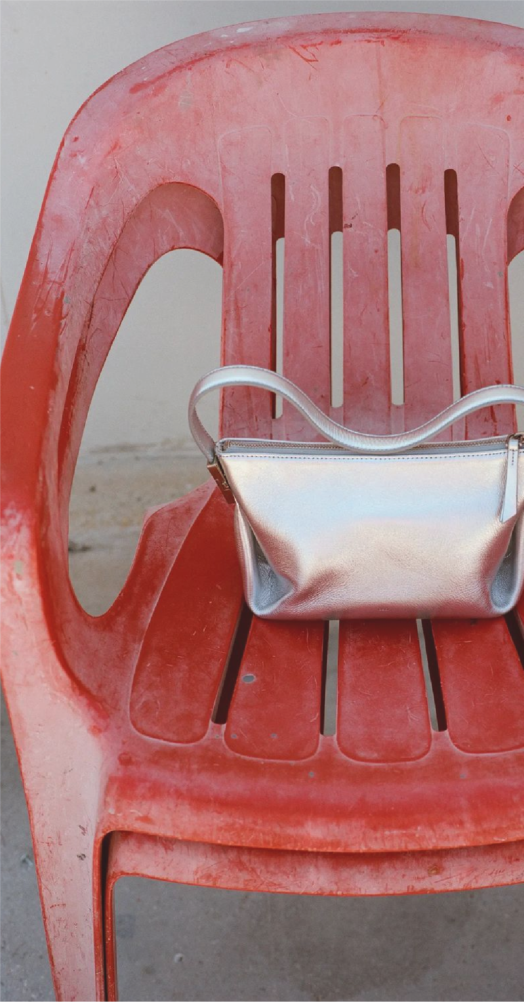 A worn red plastic chair with a shiny silver handbag resting on it.