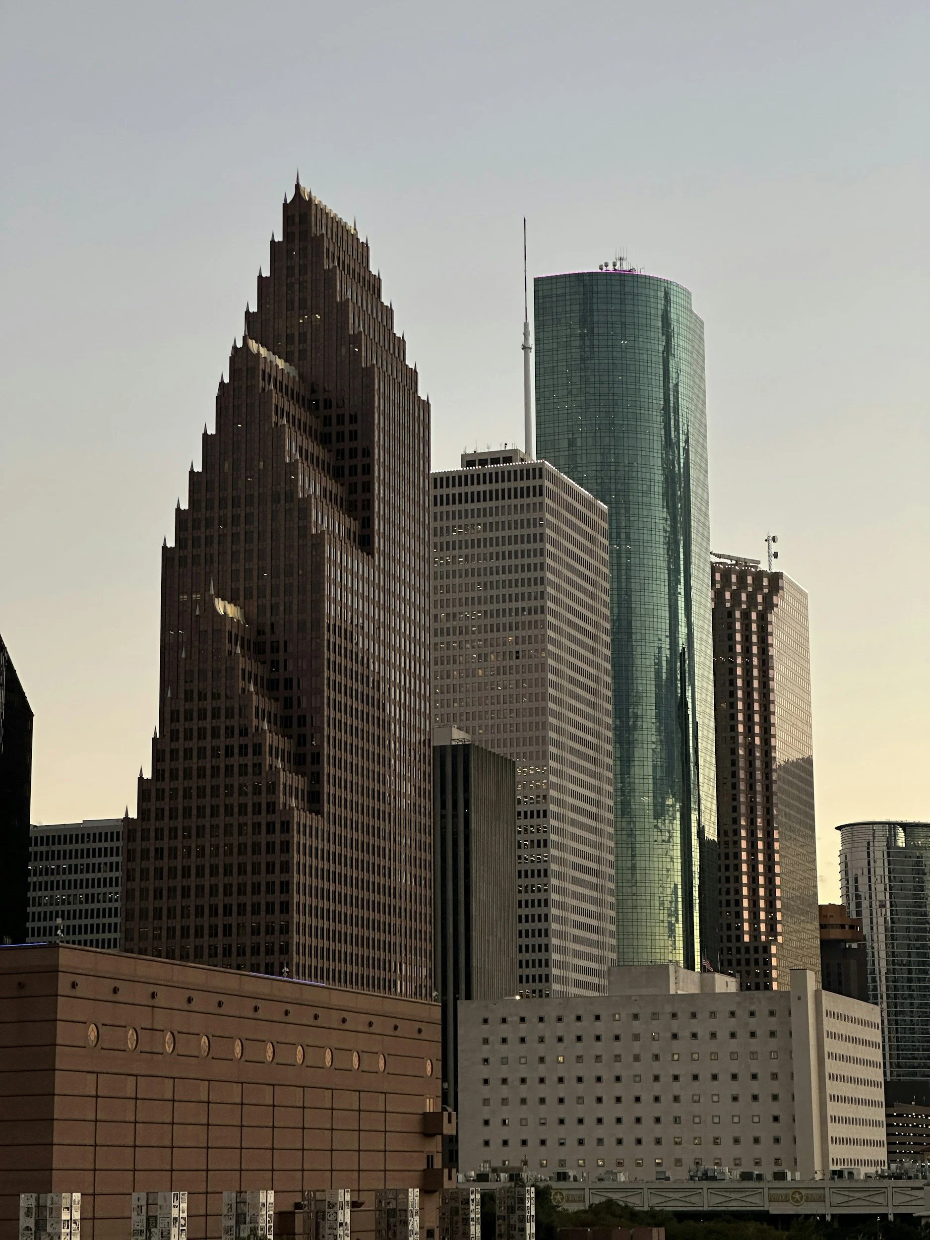 Skyscrapers in downtown with a brown, uniquely designed high-rise on the left, a glass tower on the right, and several other high-rise buildings in between, under a clear sky.