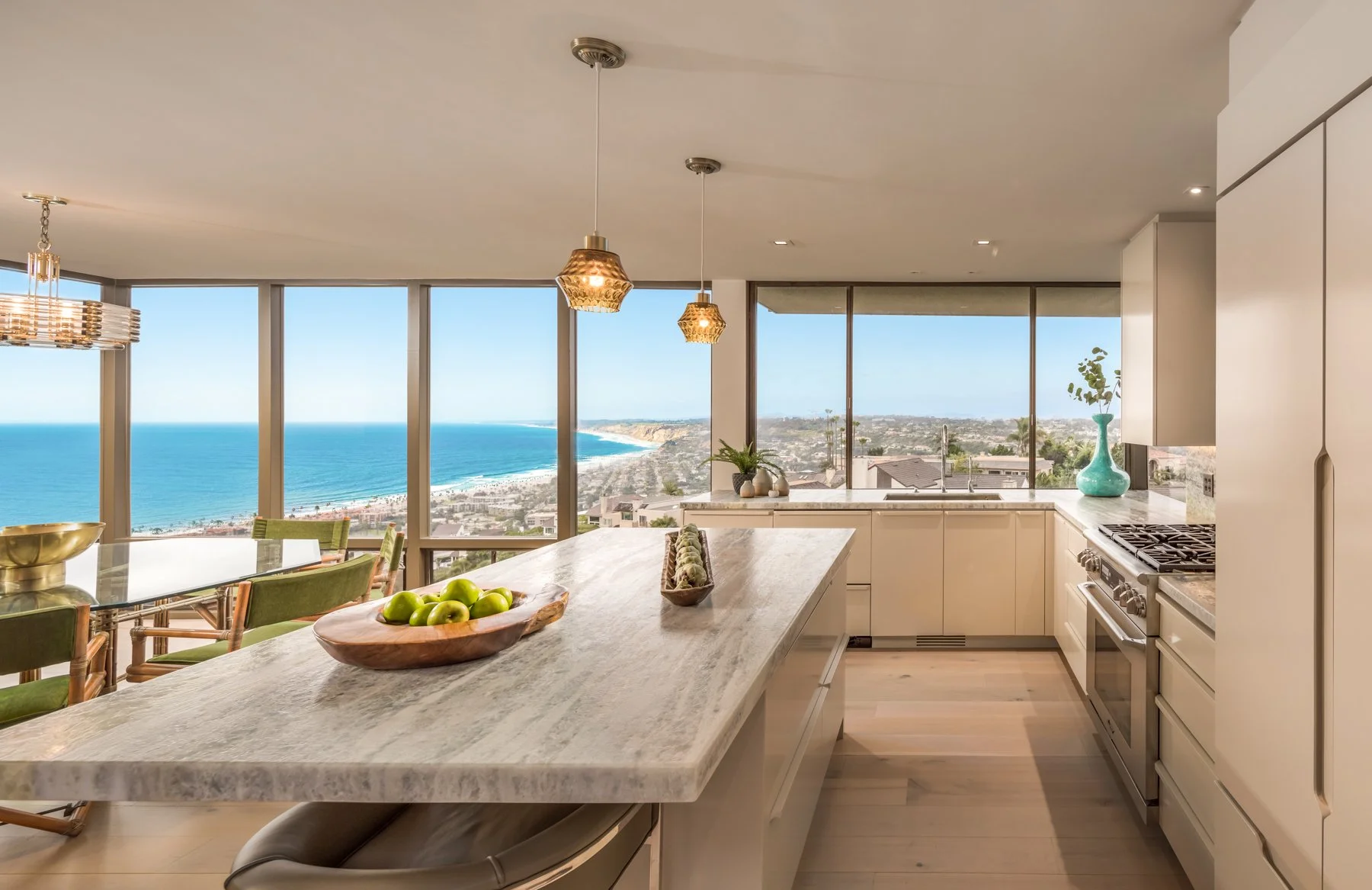 Modern kitchen in Bird Rock, California designed by Tosti Design with marble island, view of the ocean and coastline through large windows, white cabinets, and decorative vases.