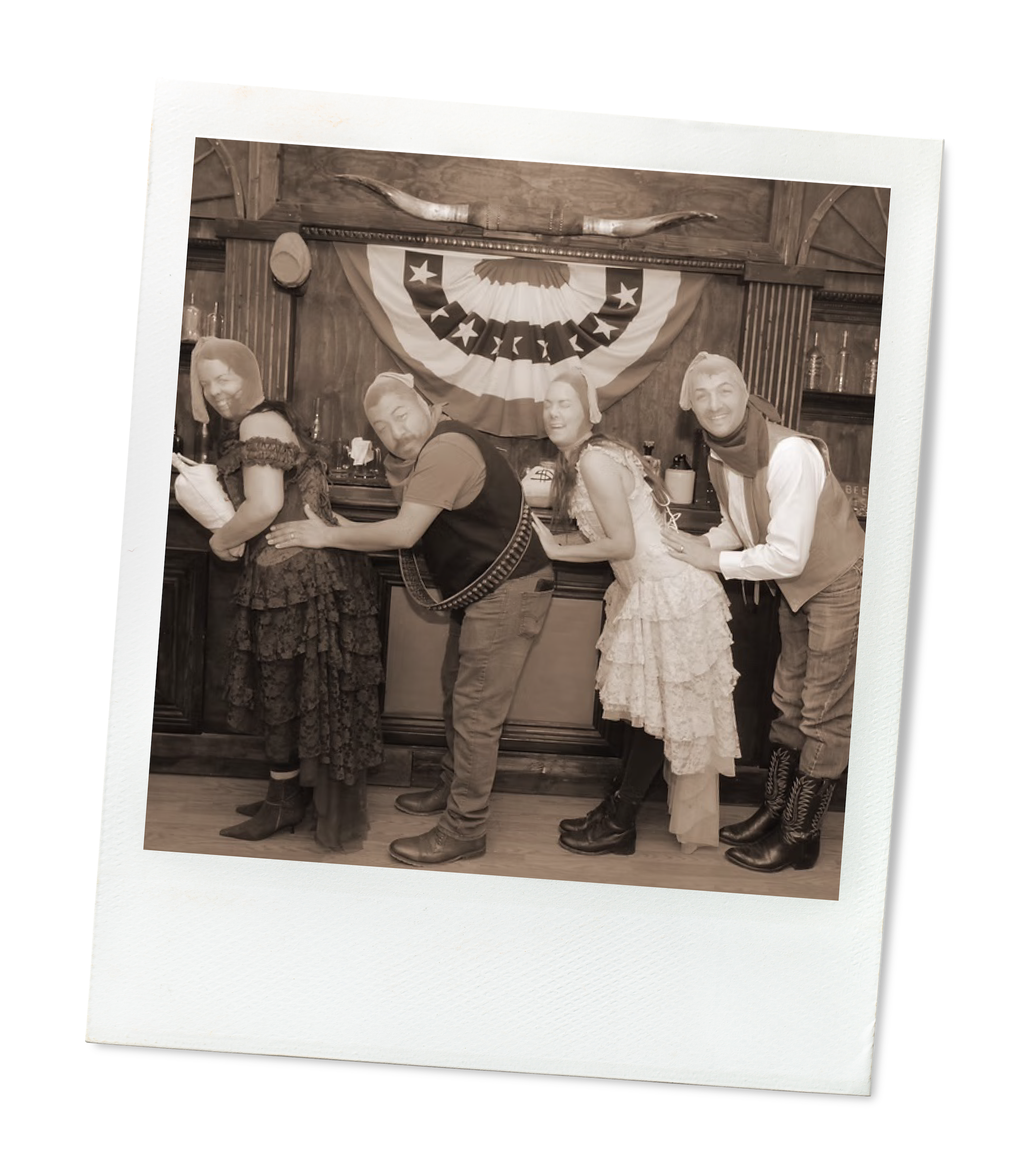 Tosti Design team dressed in Western and country-themed costumes are in a line, with their hands on the person in front of them, inside a bar with a rustic wooden background and an American flag-themed decoration above.