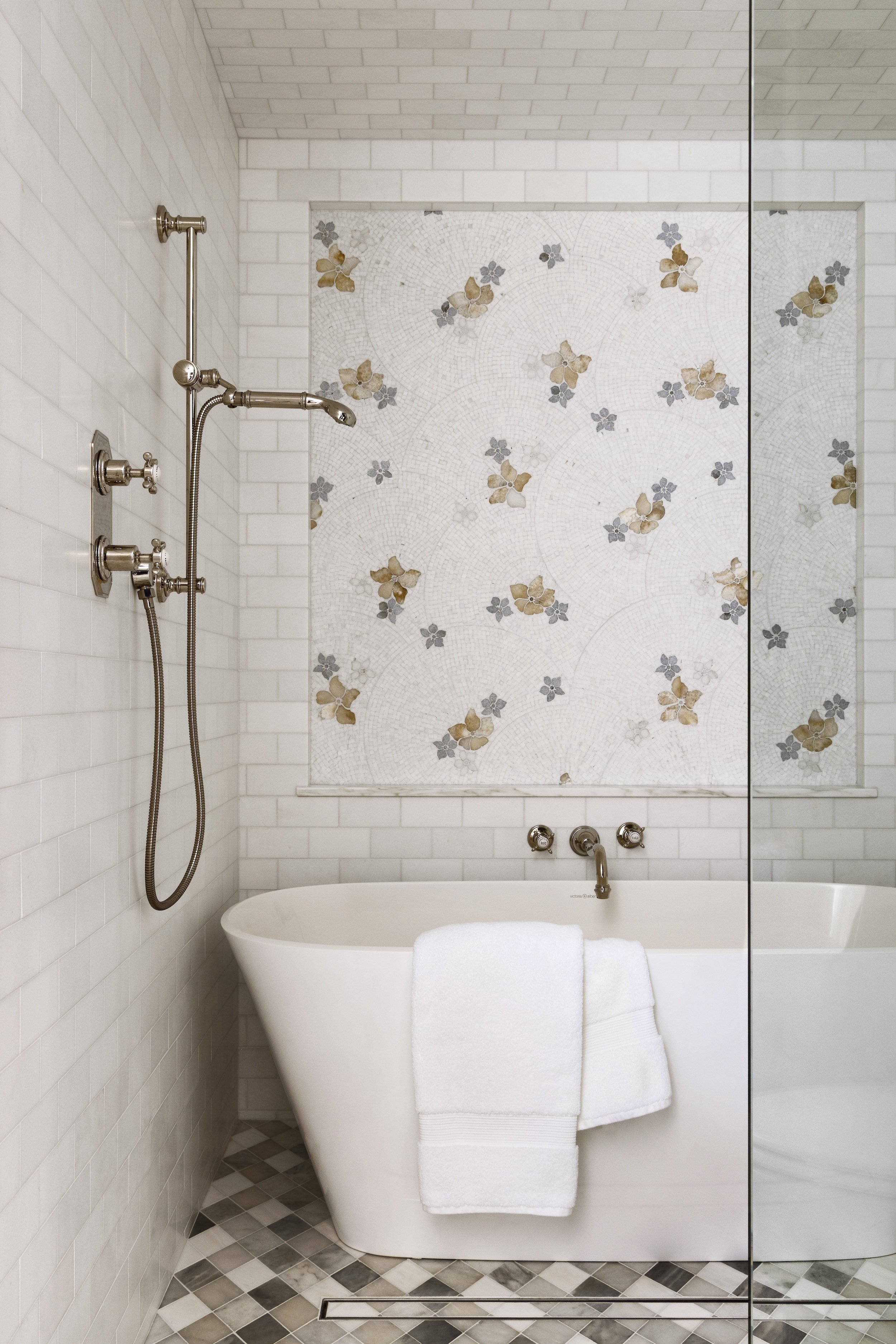 A bathroom designed by Tosti Design with a clawfoot tub, white towels, and a mosaic tile wall with floral designs.