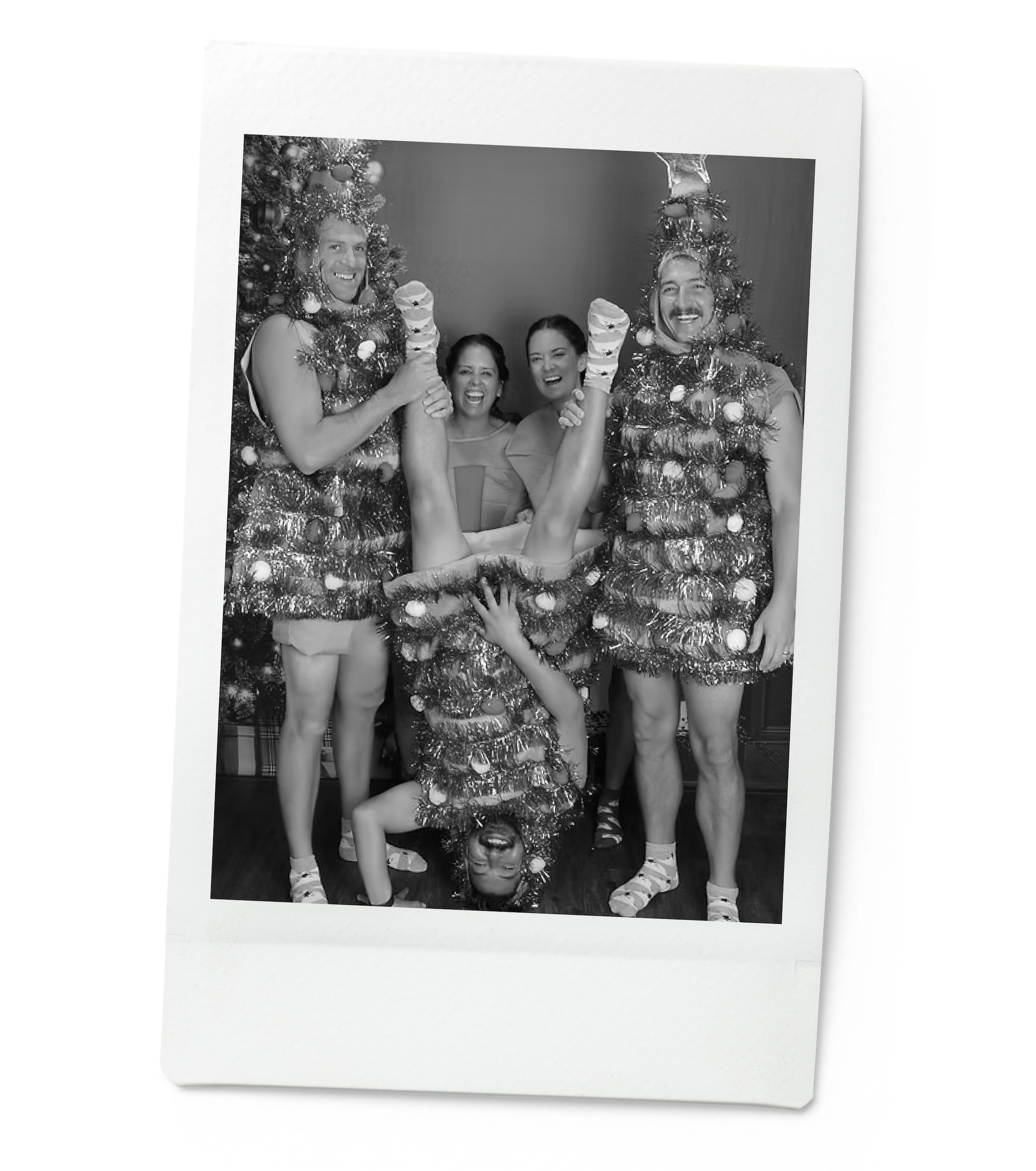 Tosti Design team dressed as Christmas trees and elves, posing for a photo in a photo booth, with one person hanging upside down and another person holding one of the upside-down person's legs.