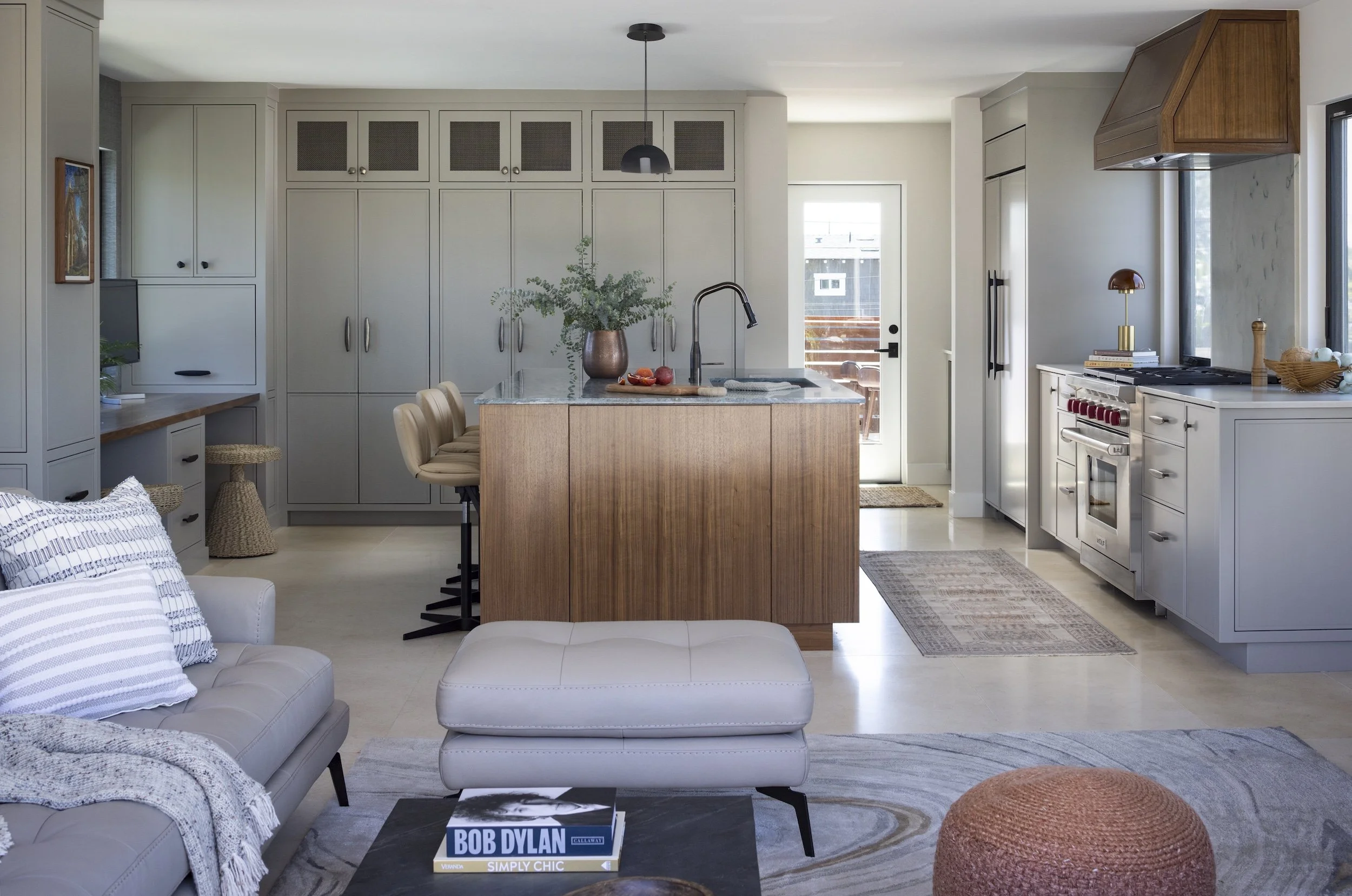 Modern open-concept kitchen and living room by Tosti Design with a kitchen island, white and gray cabinets, a stainless steel fridge, stove, and a small sitting area with a sofa and ottoman.