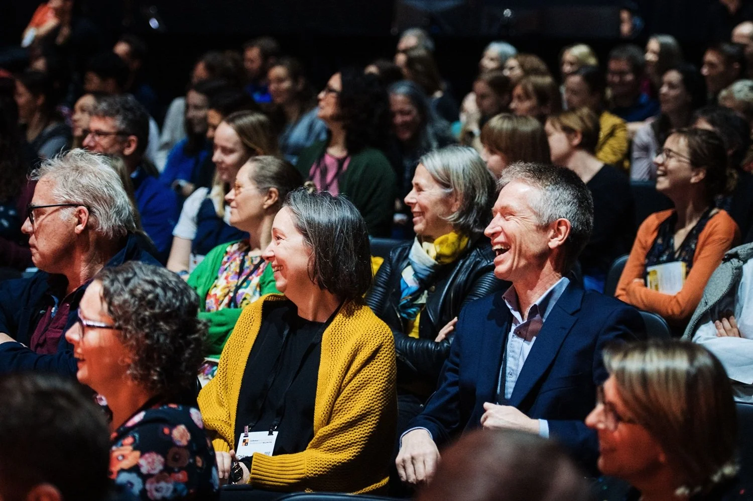 Conference attendees sitting and laughing during a keynote presentation.