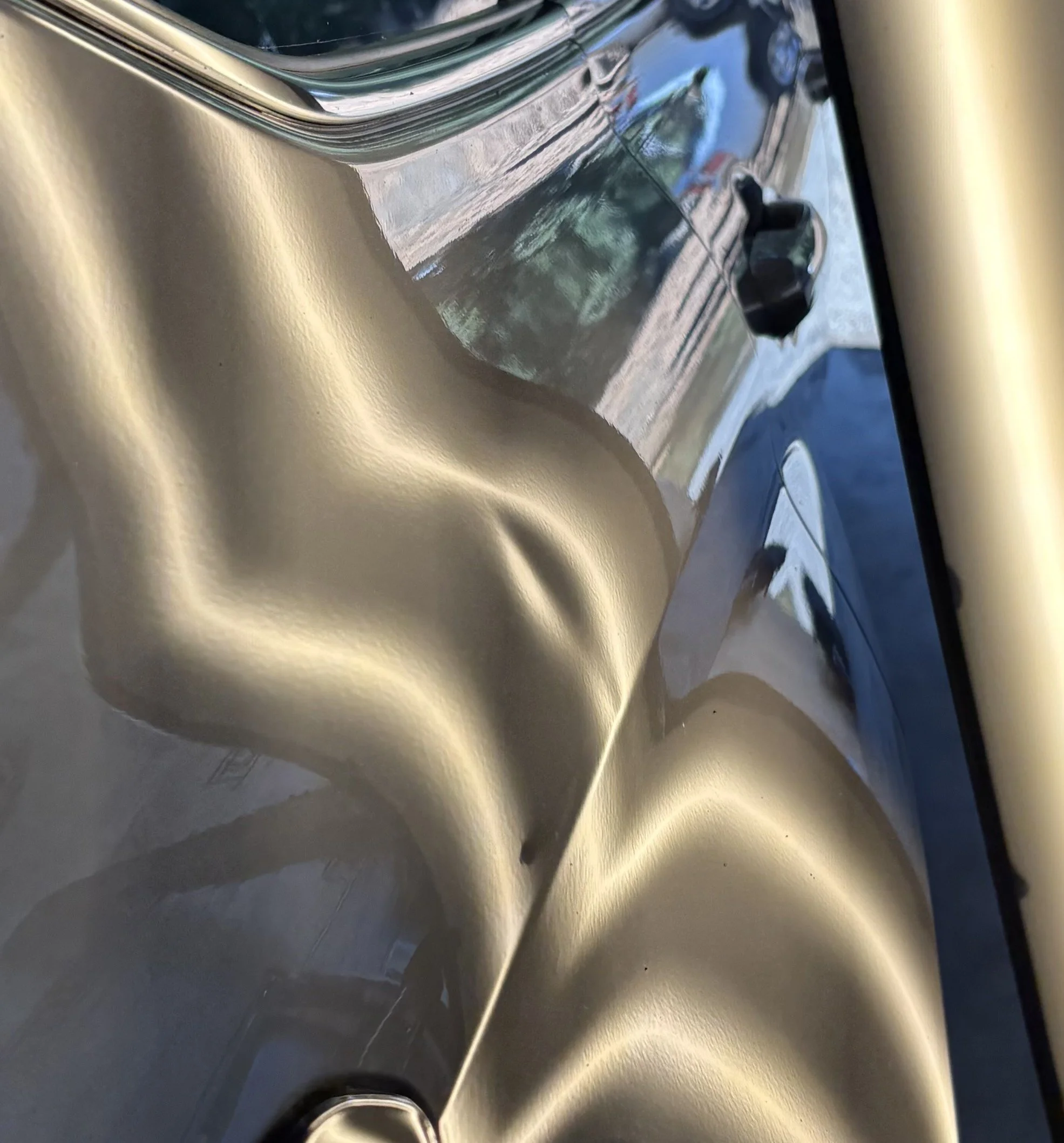 Close-up of a metallic gold-colored car with a shiny, reflective surface, showing the fender and door area.