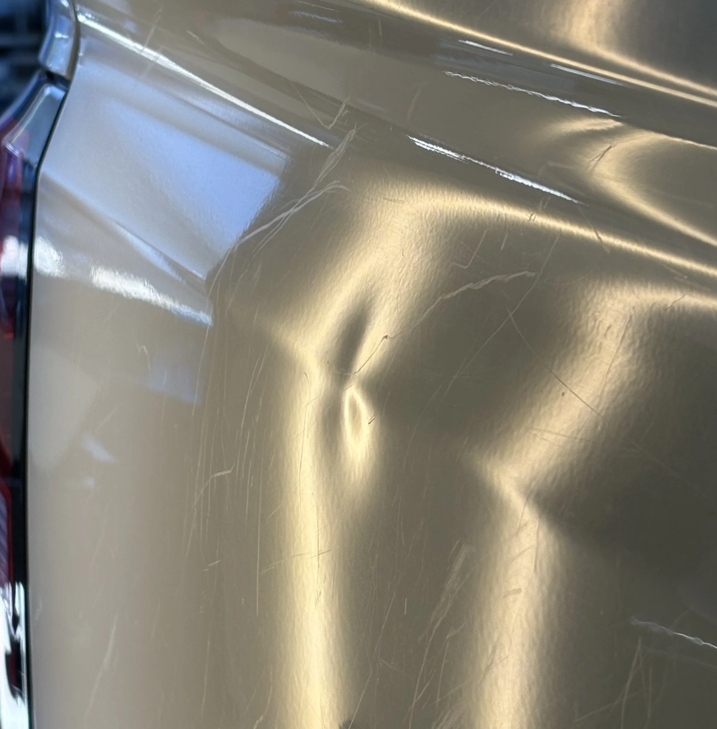 Close-up of a gold-colored metallic truck tailgate with visible scratches and a dent.