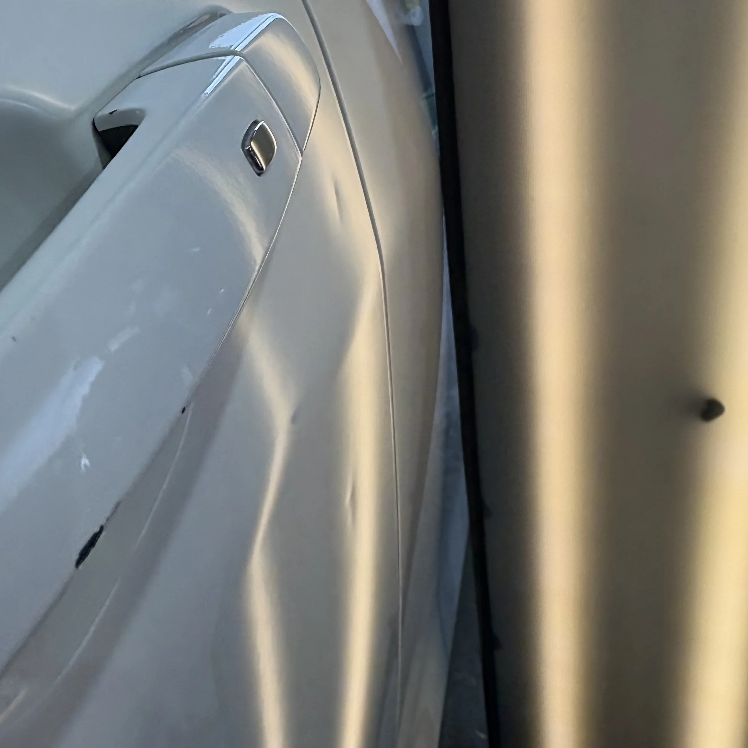 Close-up view of a white car door with two dents 