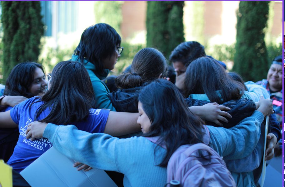 Group of young people in a tight huddle outdoors, embracing each other in a show of camaraderie.