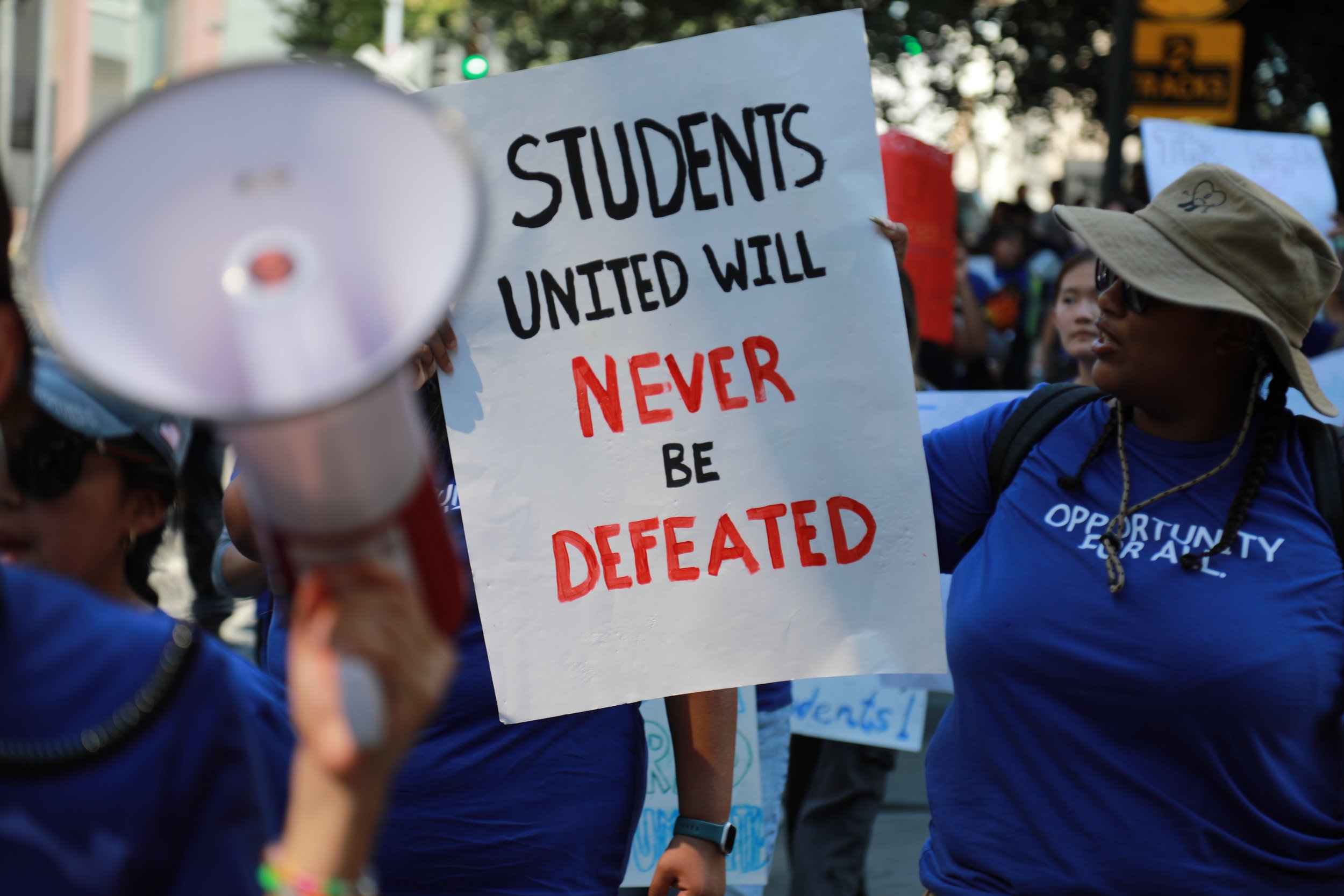 Protesters holding a sign that reads 'Students United Will Never Be Defeated' during a demonstration.